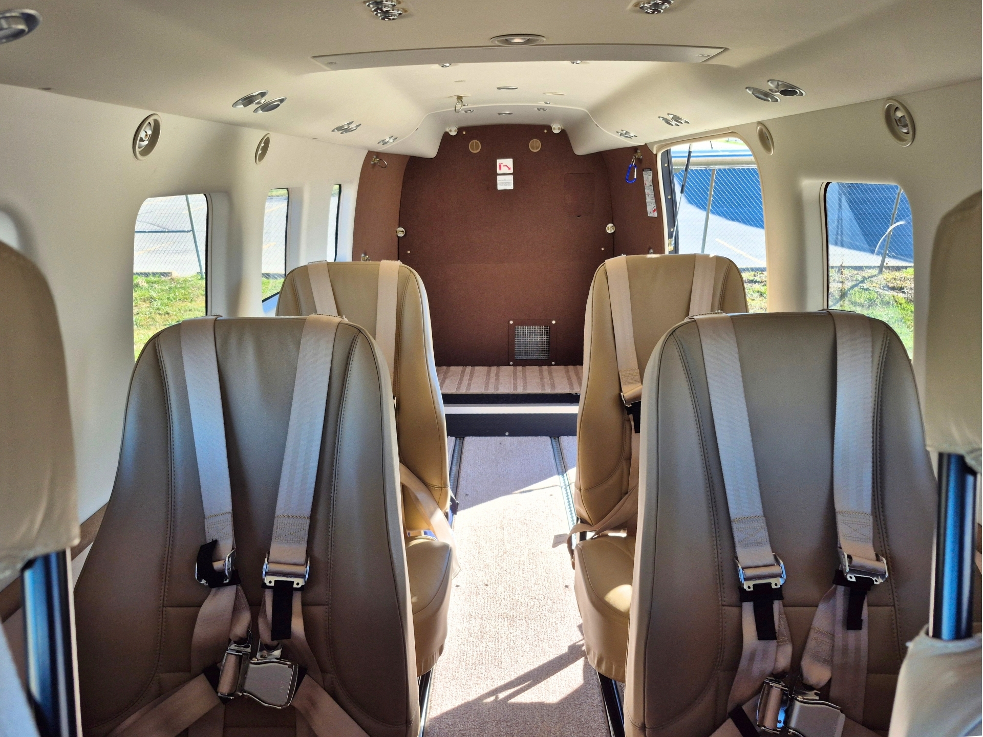 Interior of a small private airplane cabin with tan leather seats and beige walls brown aft bulkhead at the far end