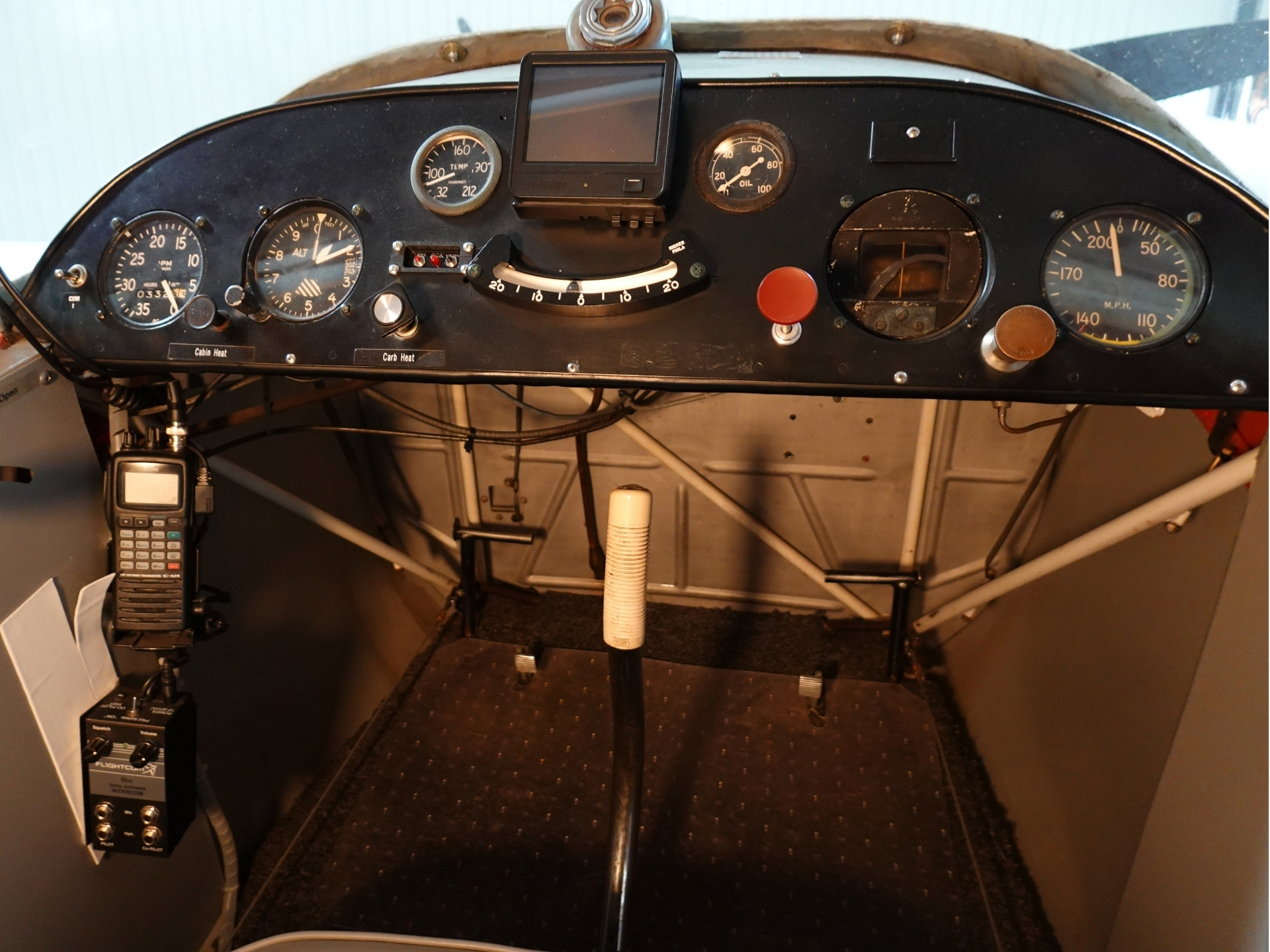 Cockpit of a small airplane instrument panel with analog gauges a mounted GPS tablet and a white center control stick in the foreground