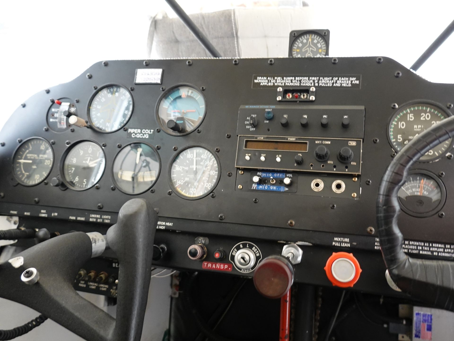 Cockpit instrument panel of a small airplane with multiple gauges, yoke, and red/orange controls visible.