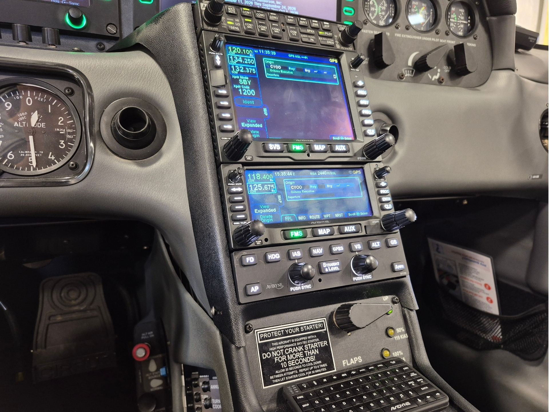 Flight deck cockpit with two blue LCD avionics screens in the center an altitude gauge to the left and multiple knobs and controls along the console