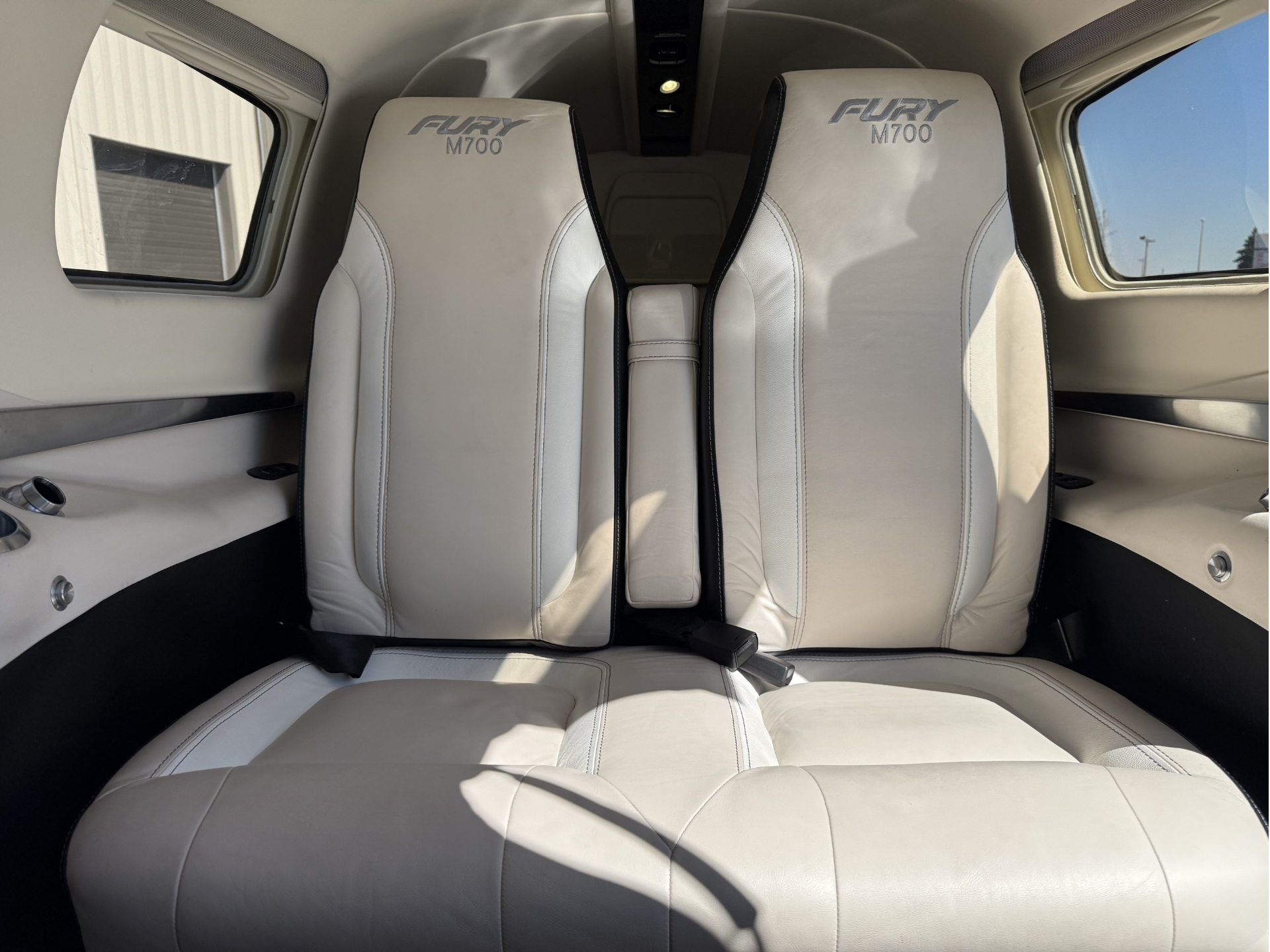 Two white leather Fury M700 aircraft seats in a private jet cabin with side windows and overhead panel visible