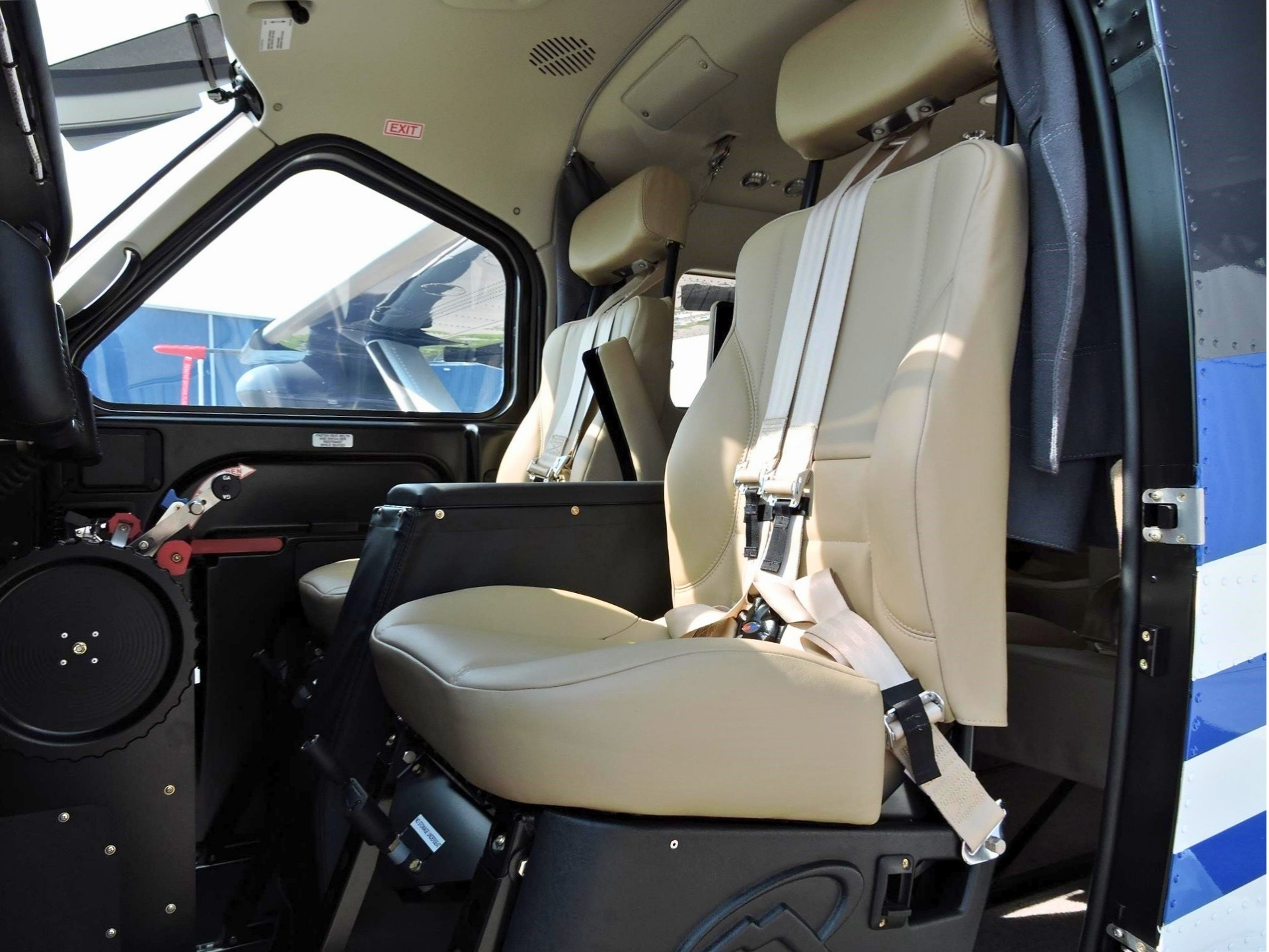 Beige helicopter cockpit seats with harnesses open door and a view of the outside runwayhangar area from the cabin