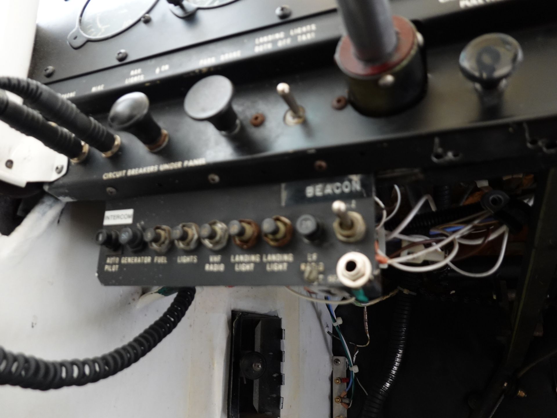 Close-up of an old electrical control panel with switches, knobs, and tangled wiring; visible labels include lamps/beacon areas on a black metal panel.