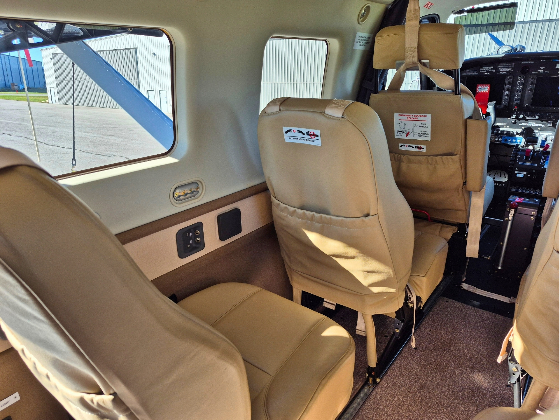Interior of a small tan aircraft cabin with beige seats window view of tarmac and wing strut visible outside
