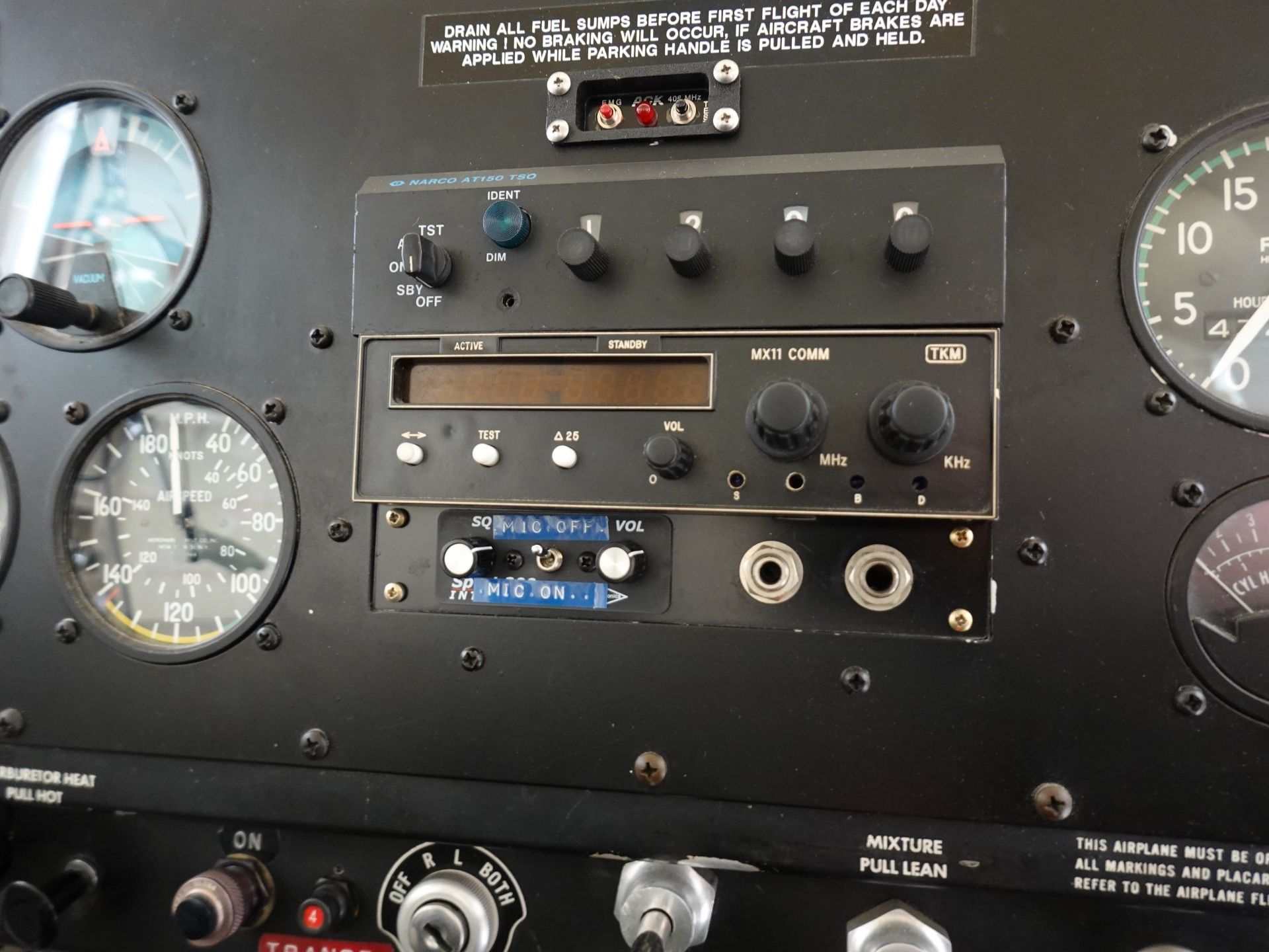 Close-up of a vintage aircraft instrument panel: left gauges include airspeed/altitude, center radios labeled MX11 COMM with knobs, and several switches and dials across the panel.