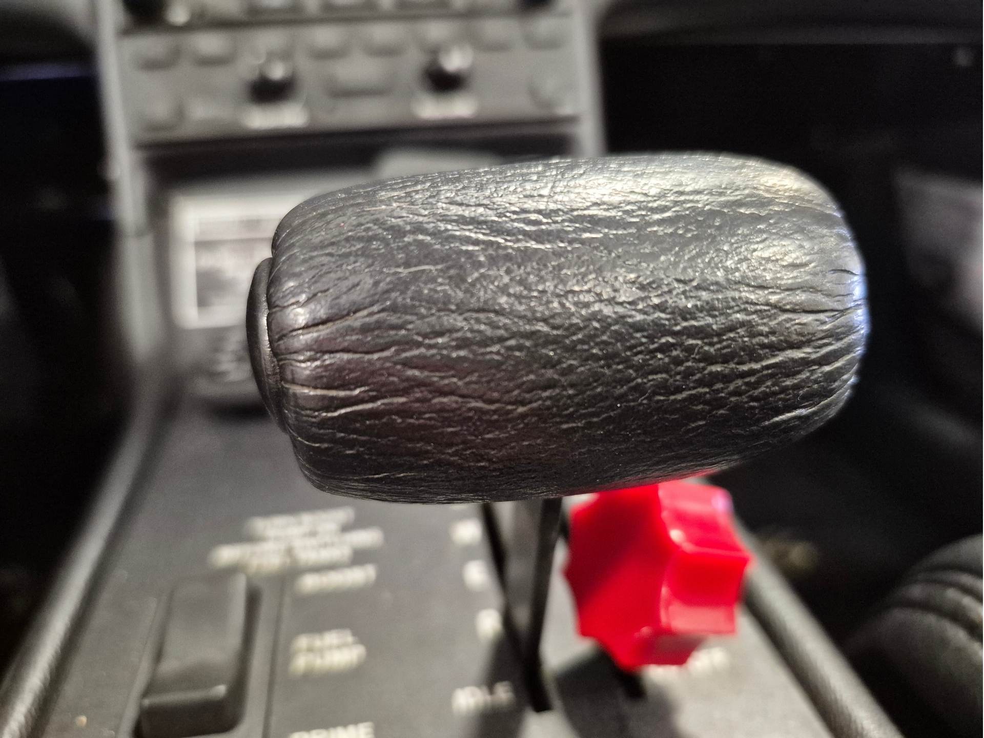 Close up of a textured black lever knob on a vehicles control panel with a red switch visible in the background