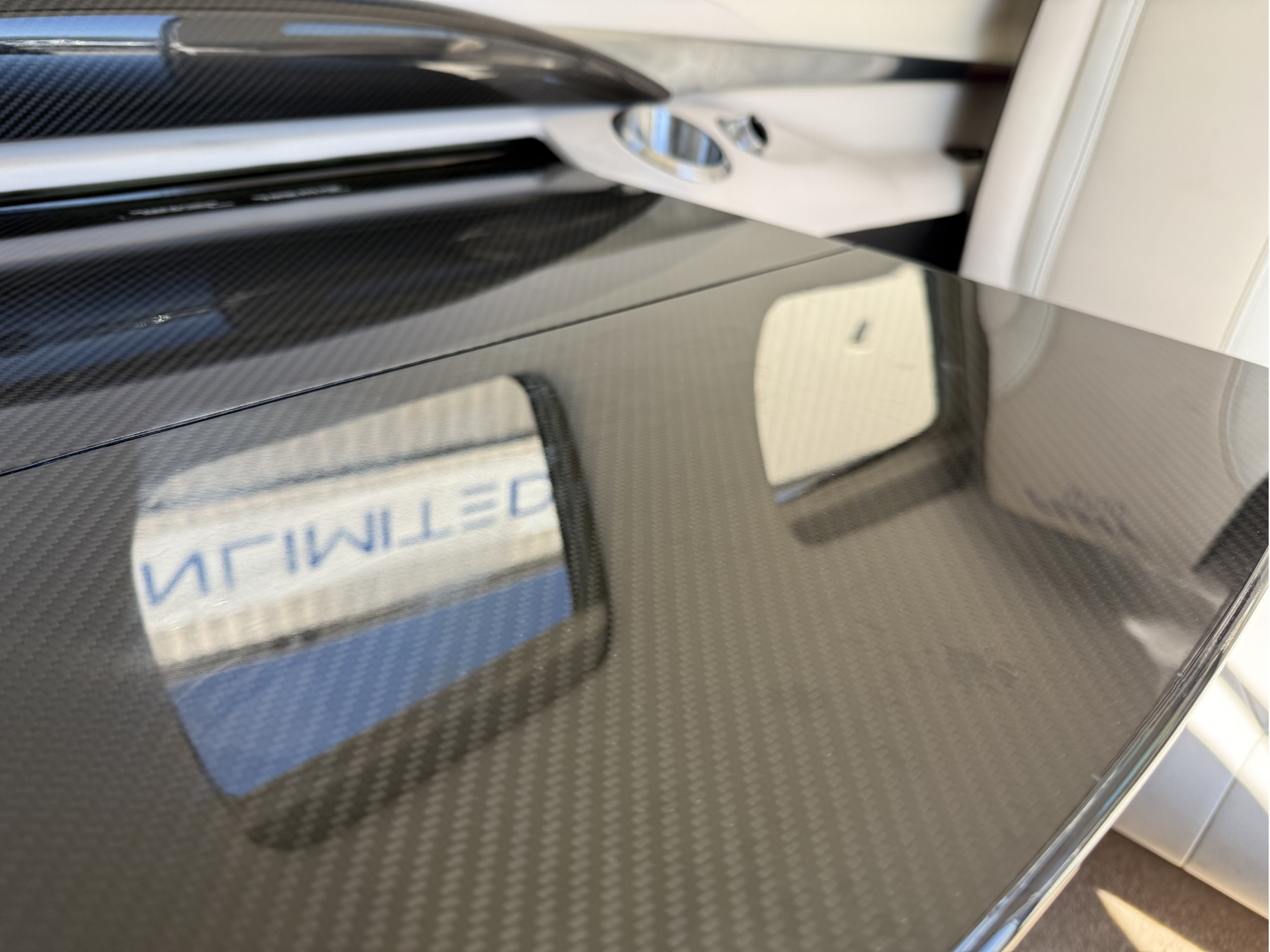 Close up of a glossy carbon fiber car surface with a chrome door handle and a reflected word LIMITED seen in the sheen