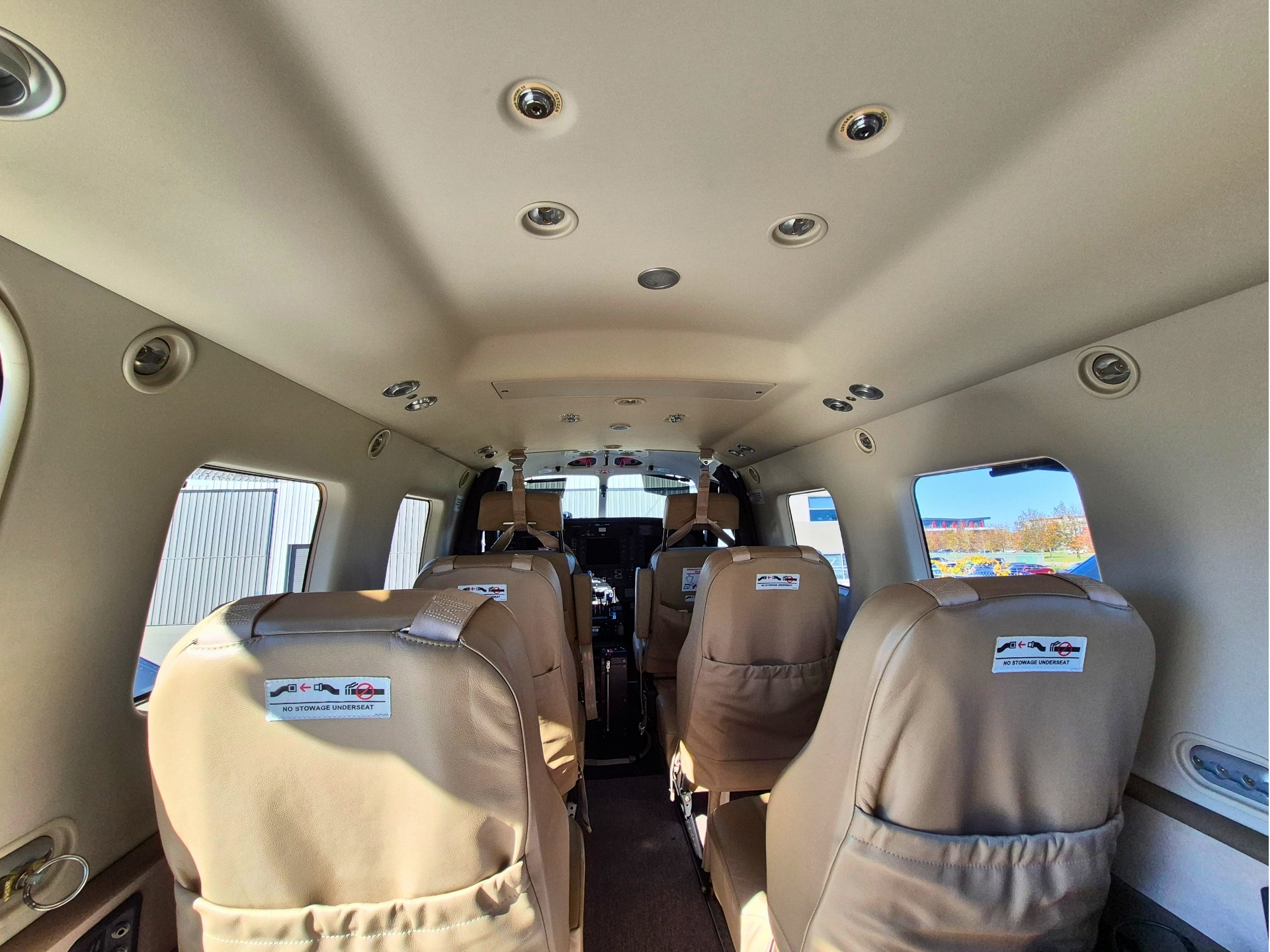 Interior of a small aircraft cabin with beige seats ceiling mounted lights and side windows showing an airport outside