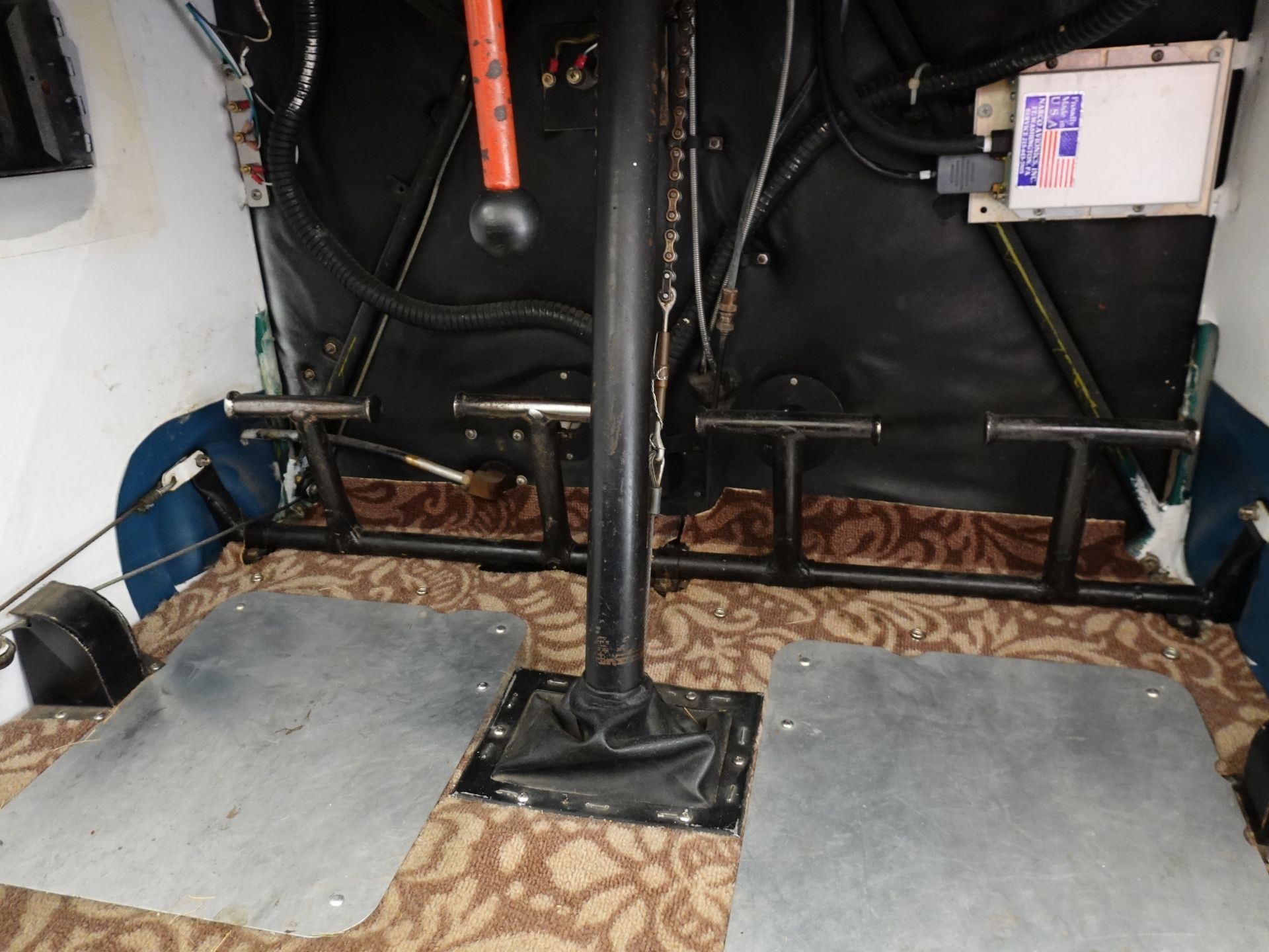 Industrial interior with a central vertical support column, exposed cables, and metal framing on a patterned brown floor mat.