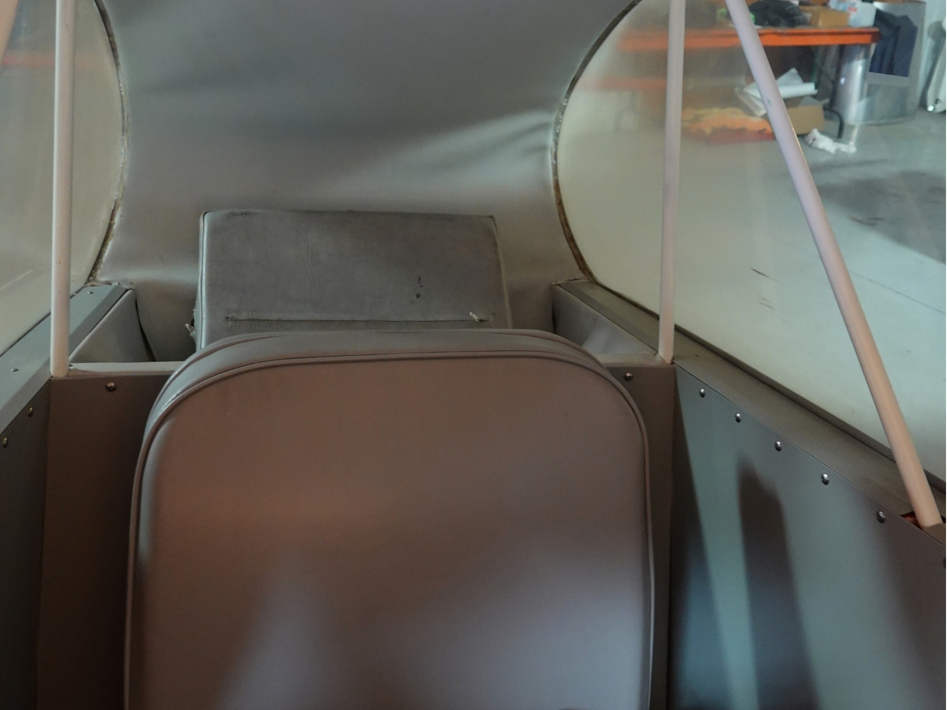 Backseat view inside a small cabin with two brown leather seats and metal panels along the sides