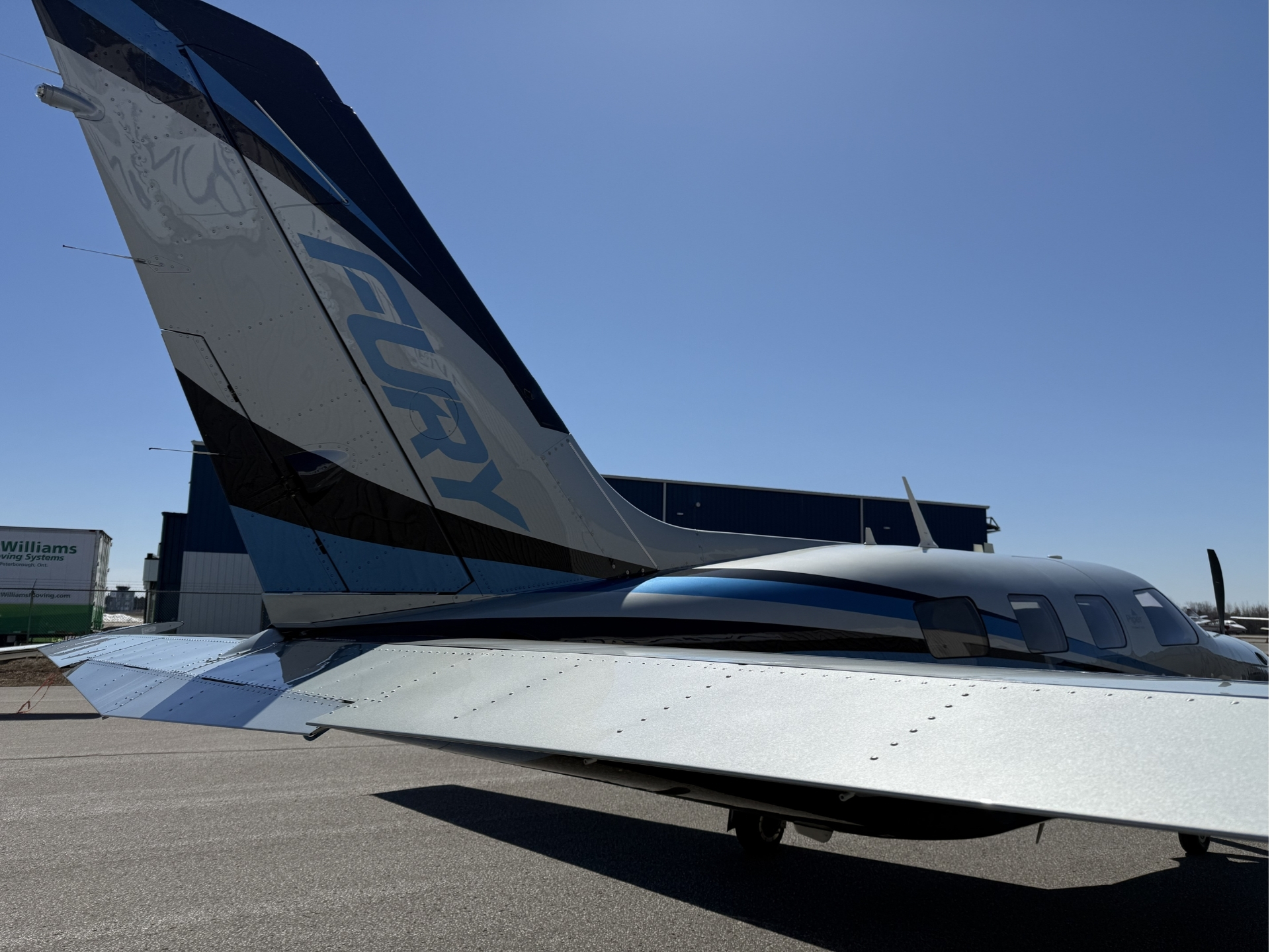Tail section of a small aircraft on the tarmac with a clear blue sky above it