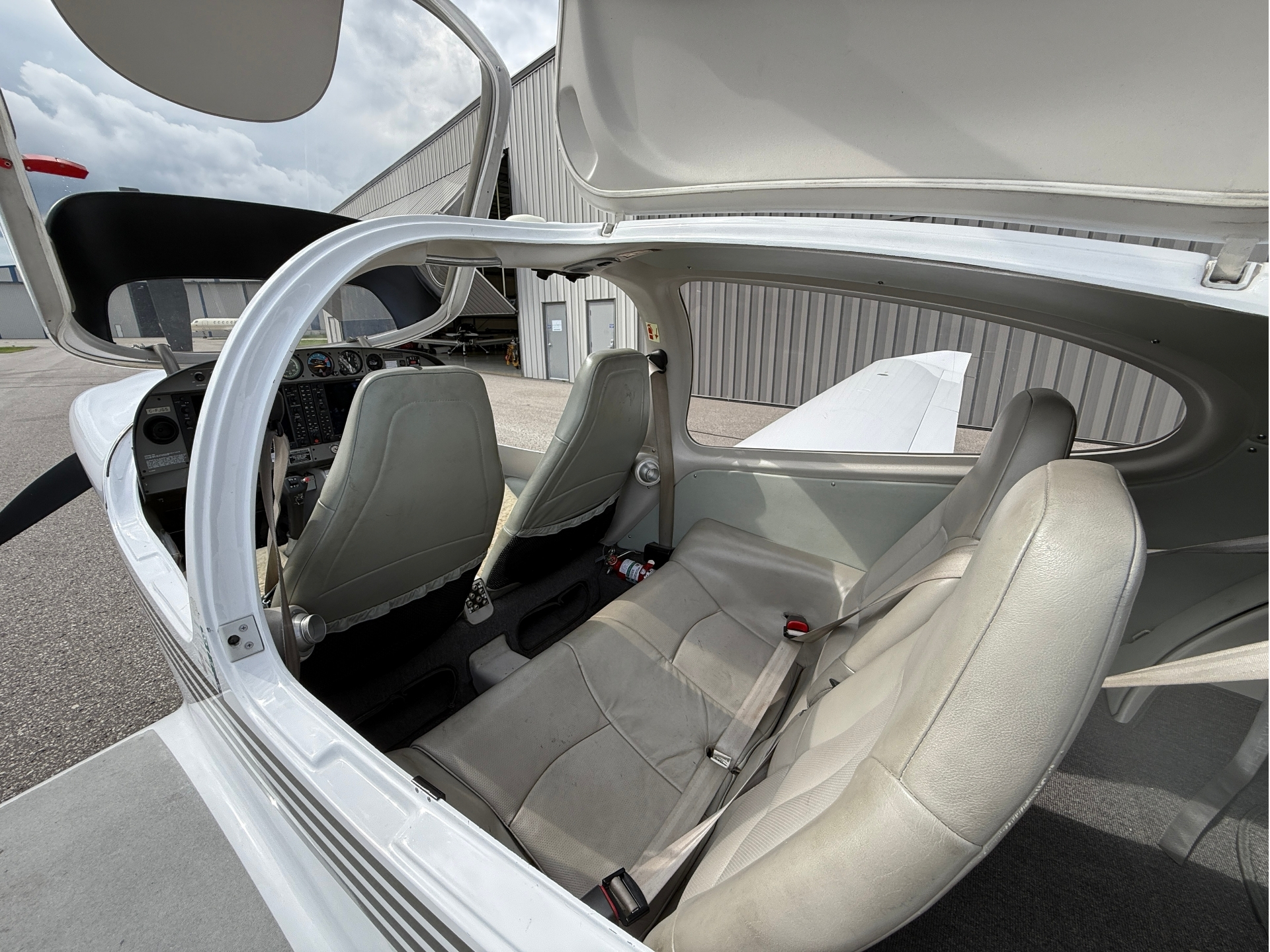 Open cockpit of a small airplane showing two beige seats and the instrument panel inside a hangar backdrop