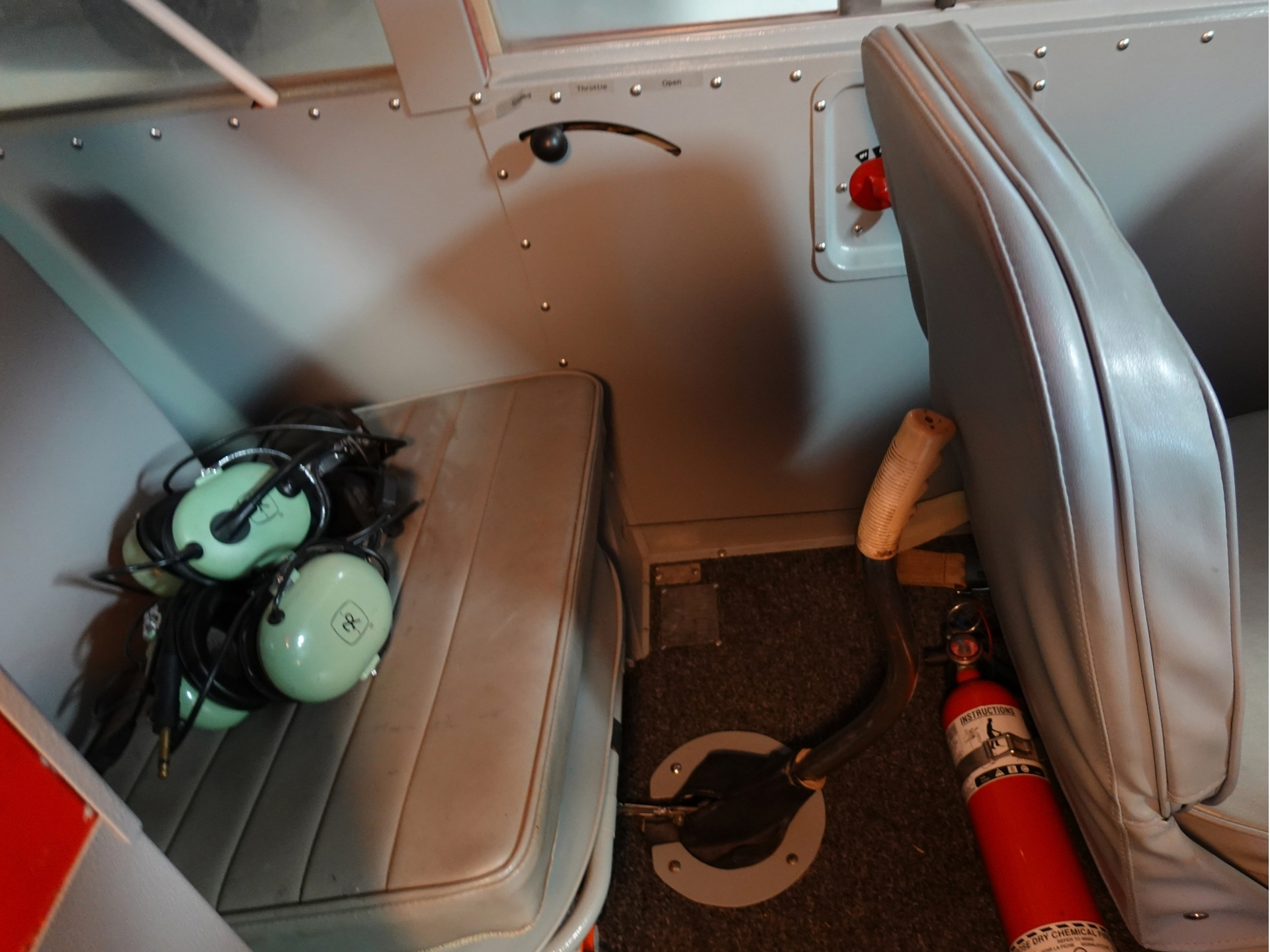 Cockpit interior with light blue seats a bundle of green aviation headsets on a bench and a red fire extinguisher nearby