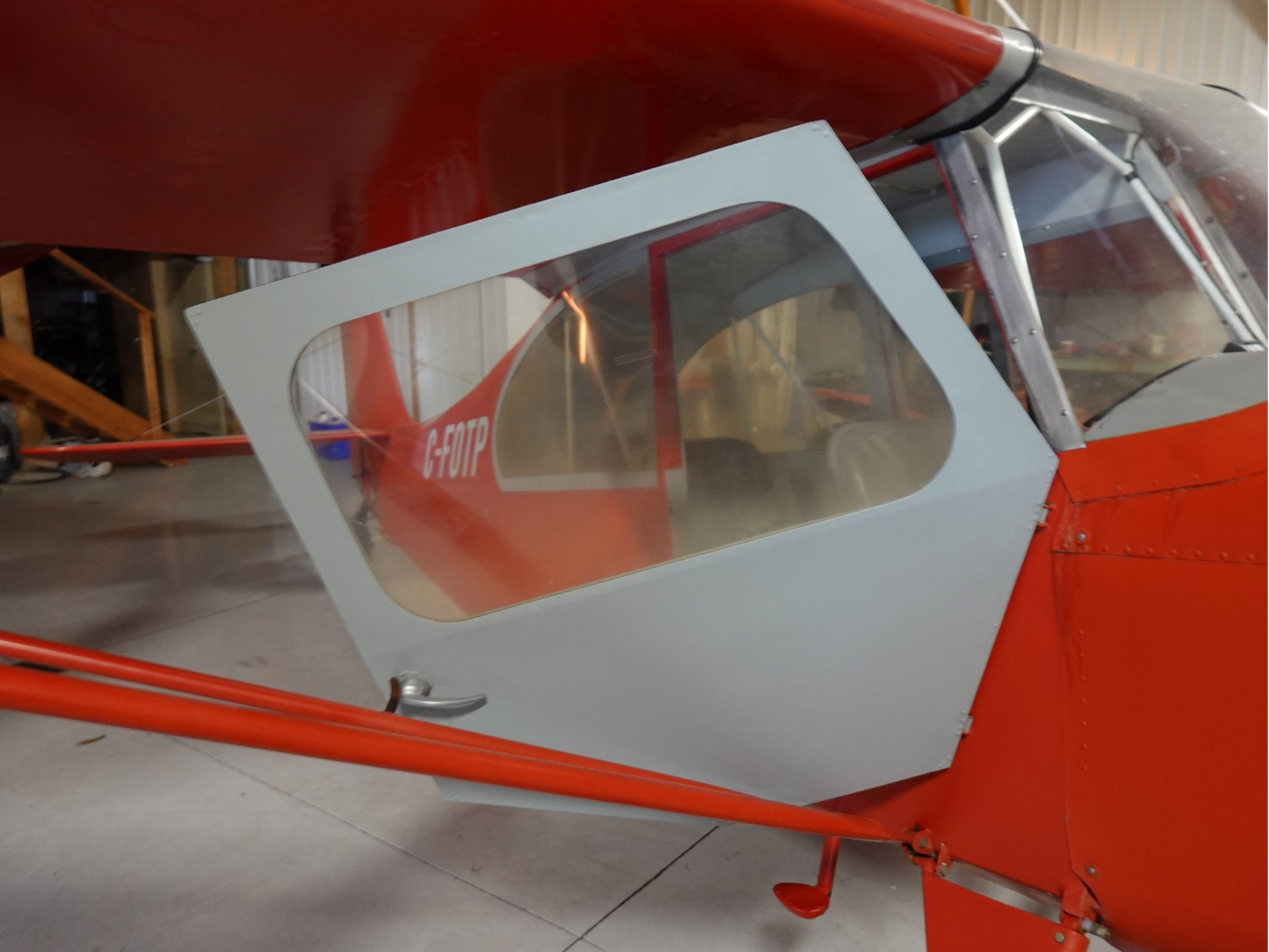 Close up of a red airplane cockpit in a hangar featuring a light gray rounded corner canopy with a large window and the registration G FOTP on the fuselage