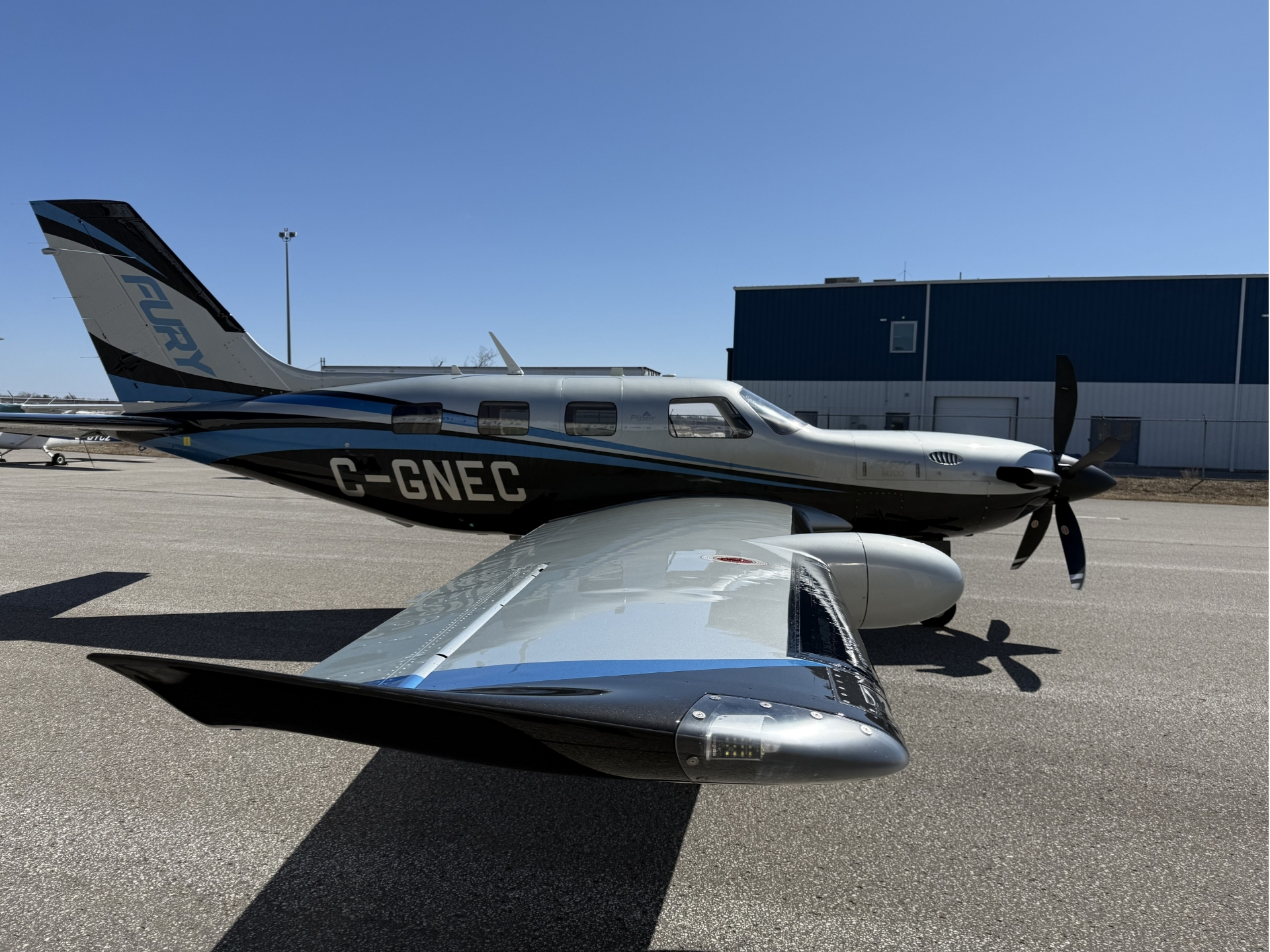 Twin engine propeller airplane on a tarmac beside a blue hangar under a clear blue sky registration G GNEC visible on fuselage