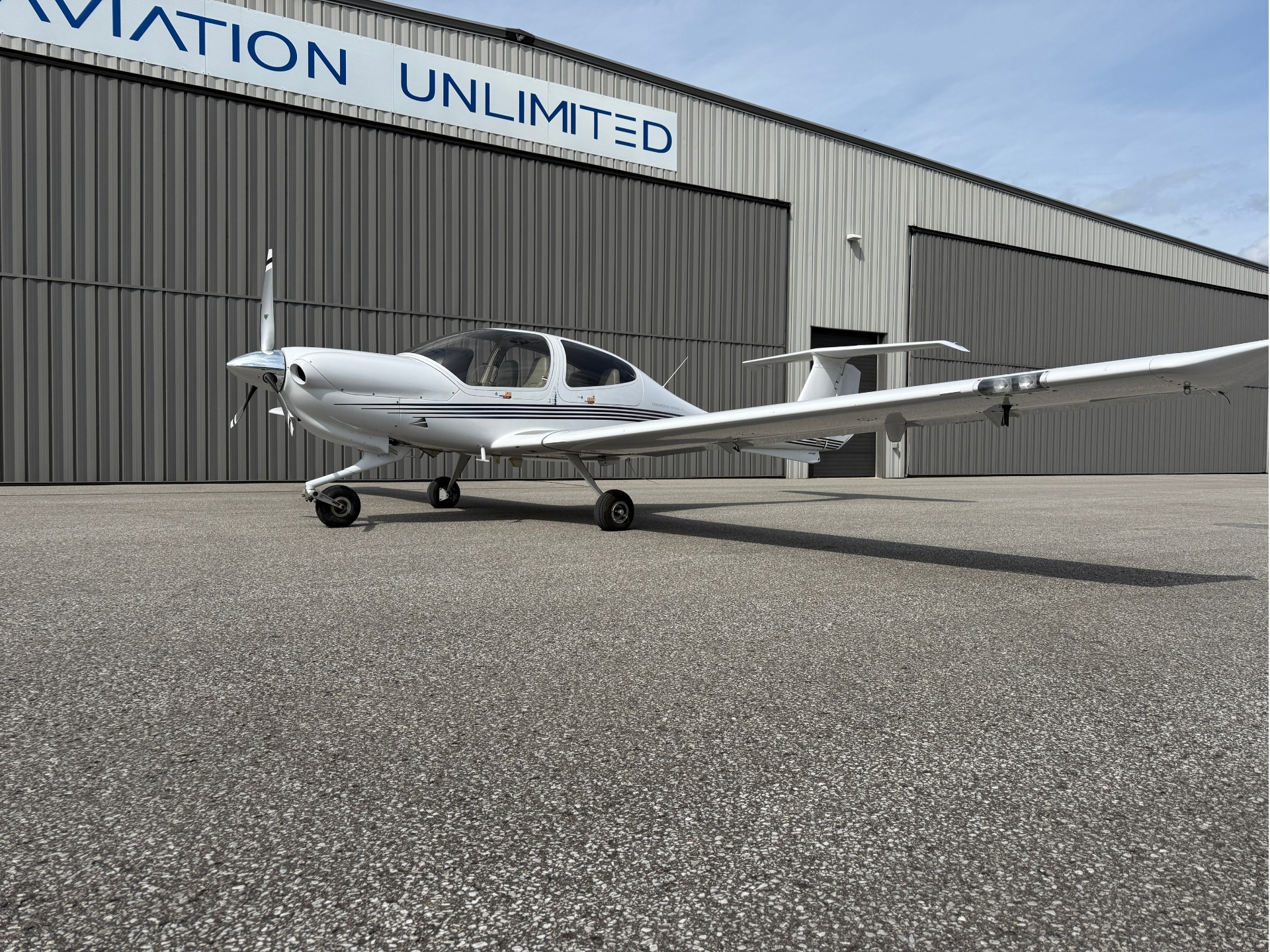 White small airplane with propeller parked on tarmac in front of a gray metal aircraft hangar with a blue sign above.