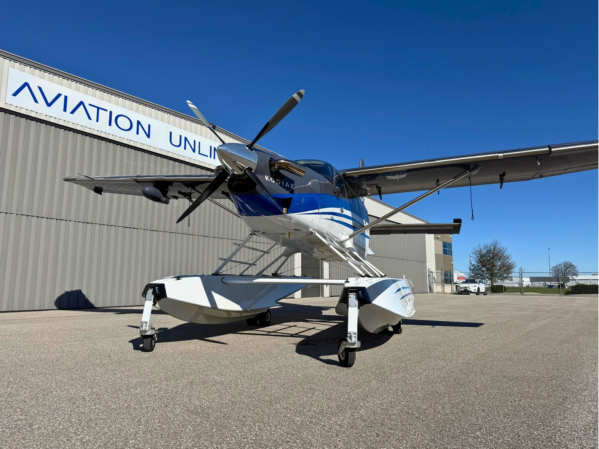 Single engine Kodiak seaplane on a wheeled float landing gear parked outside a hangar under a clear blue sky