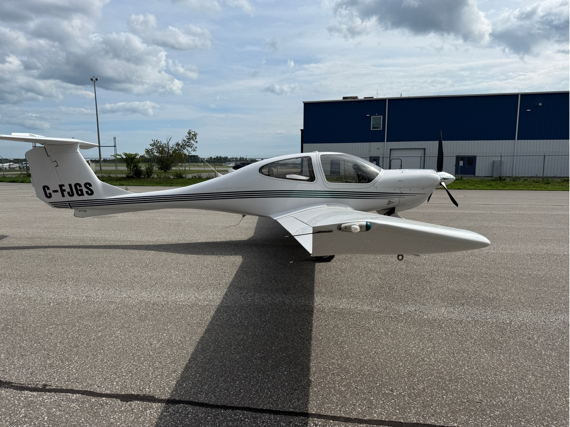White Diamond Star XL light aircraft on the tarmac, tail number C-FJGS, with blue hangar in the background.