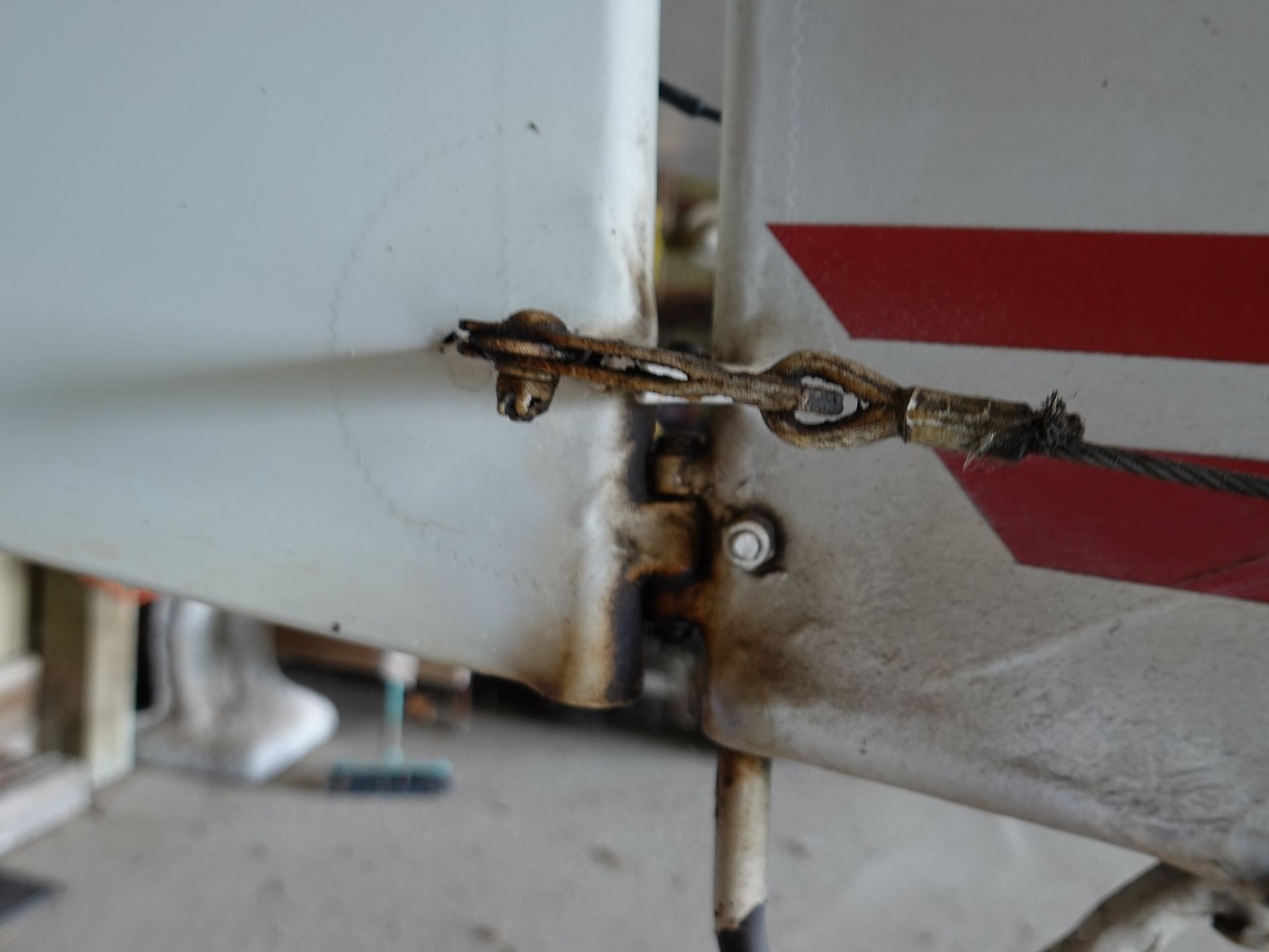 Close-up of a rusted metal hinge and frayed wire on a weathered gray surface with red diagonal stripes in the background
