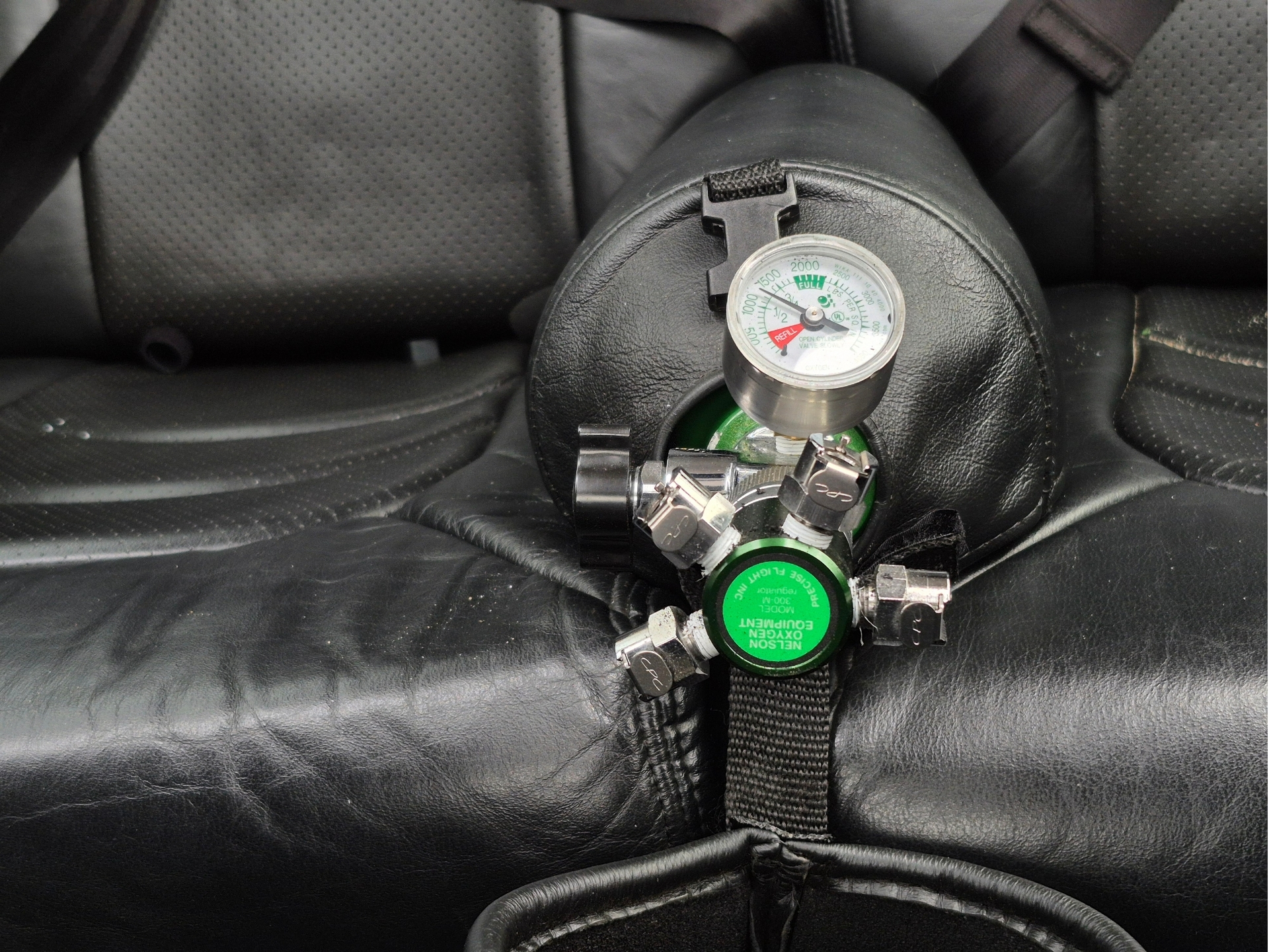 Close up of a scuba regulator and round pressure gauge connected to a green air tank on a black leather surface