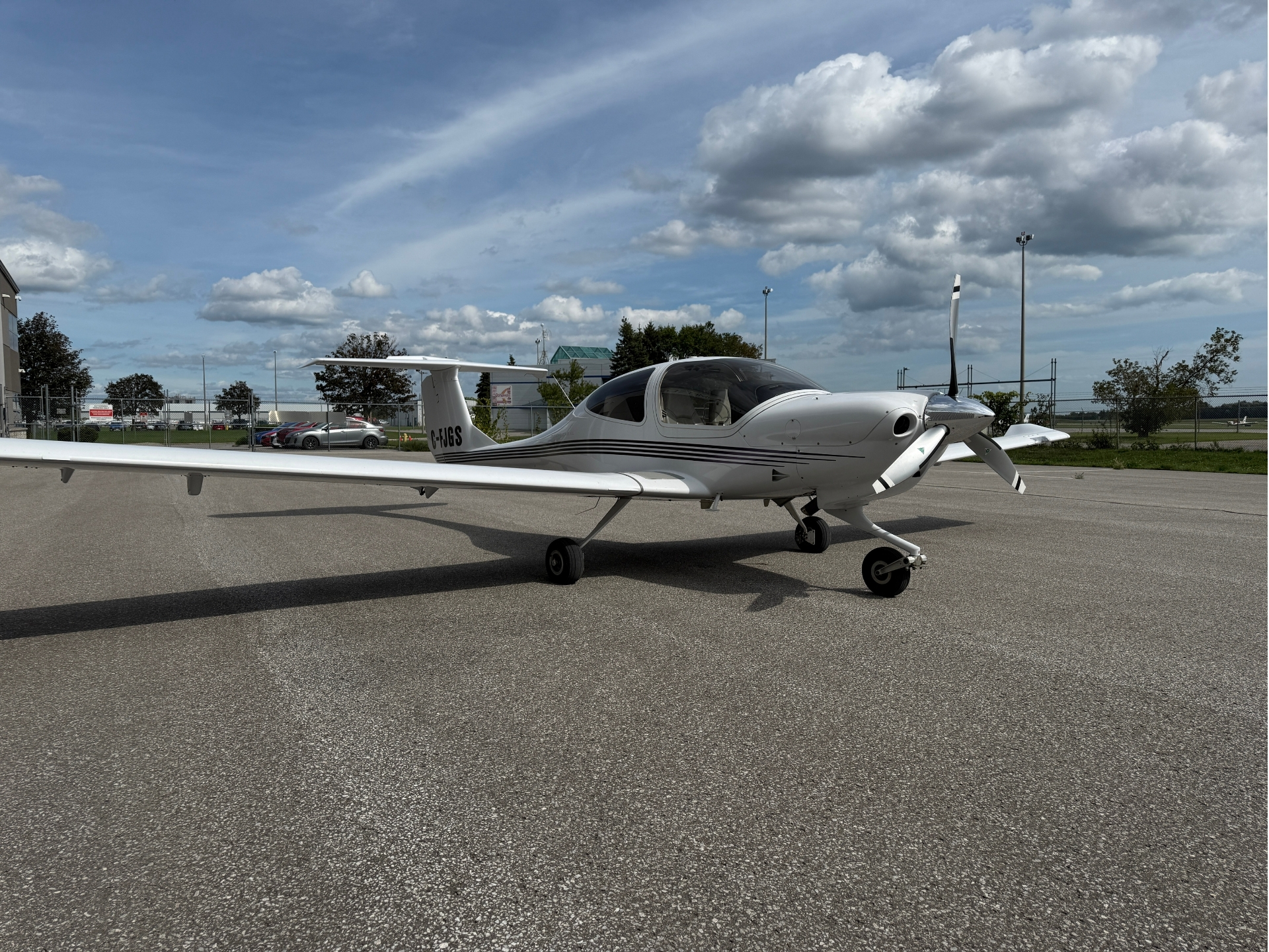 Small white light airplane parked on a tarmac under a blue, partly cloudy sky.