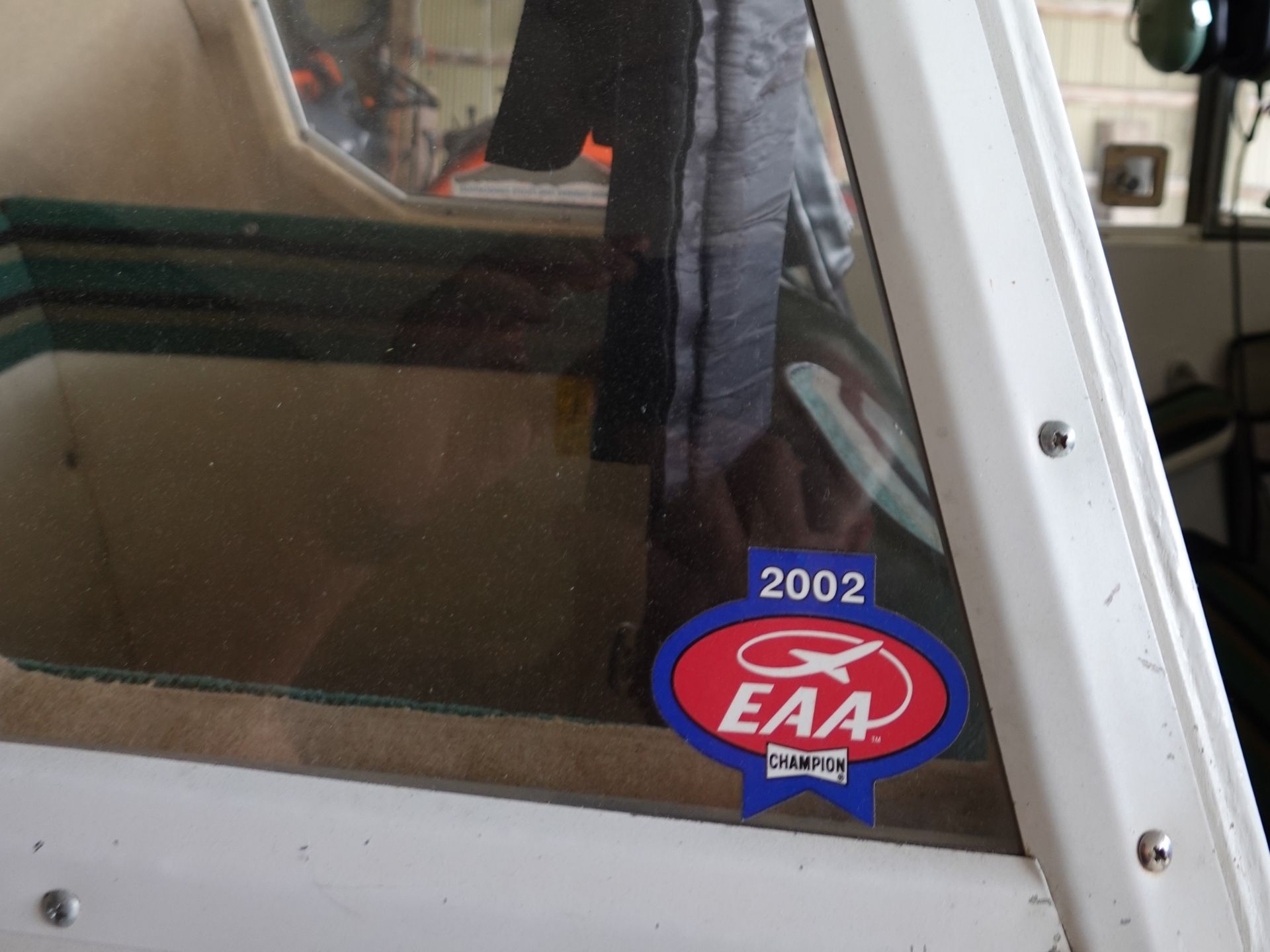 Close-up of a dusty car window with a blue EAA Champion sticker and the number 2002 visible on the glass.