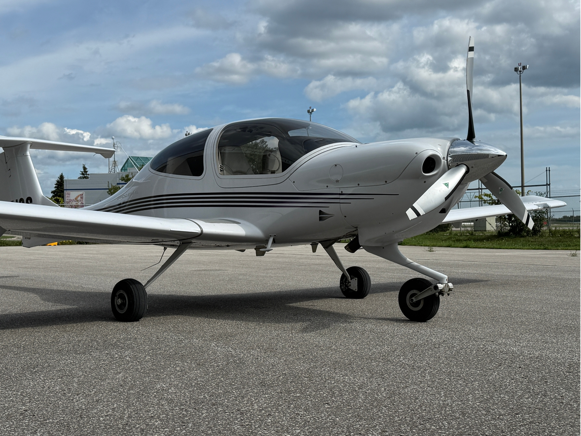 White single-engine airplane parked on a taxiway with a closed cockpit canopy and spinning propeller visible at the nose.