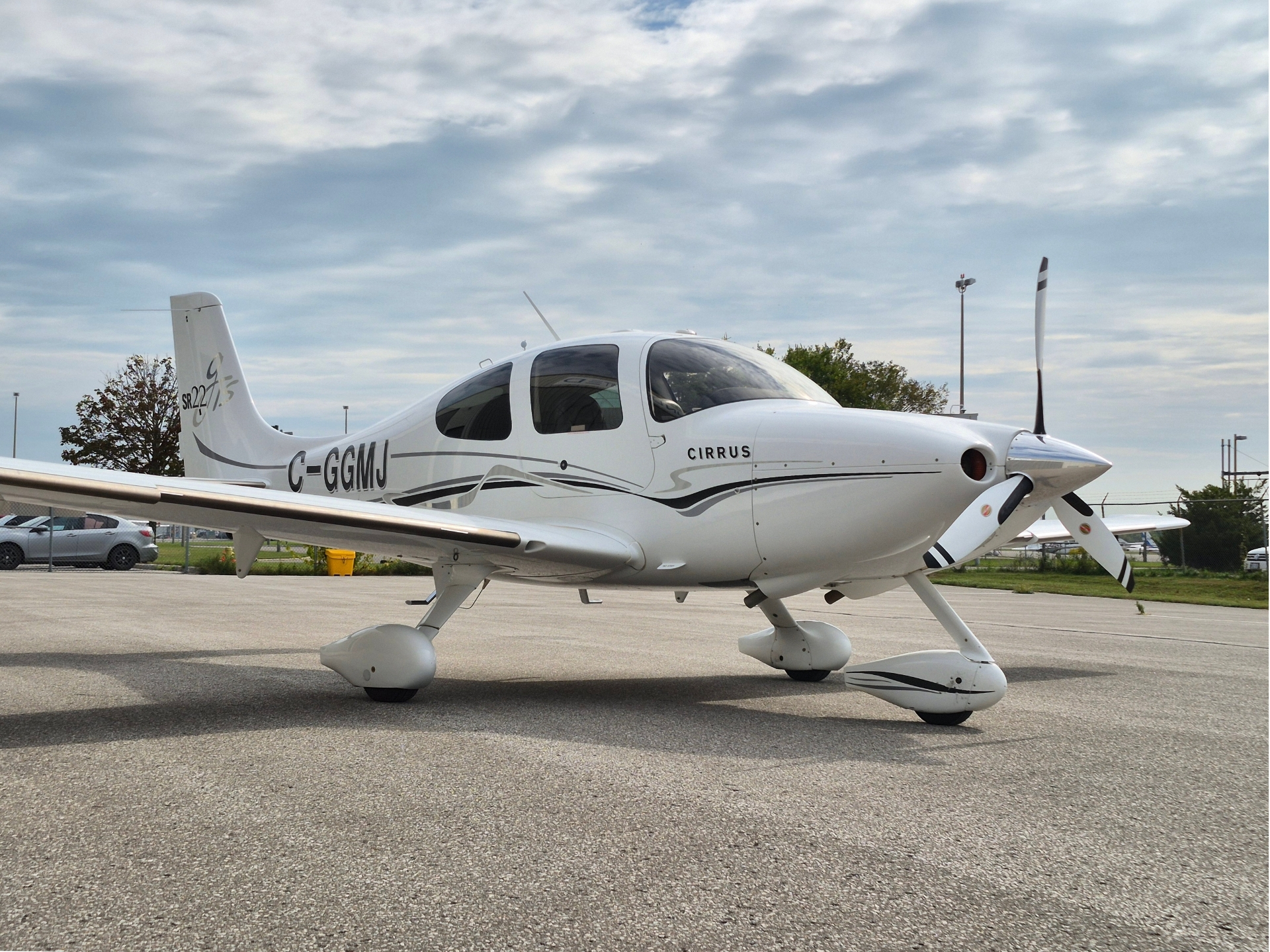 Small white Cirrus single engine airplane parked on a tarmac propeller at the nose and landing gear visible