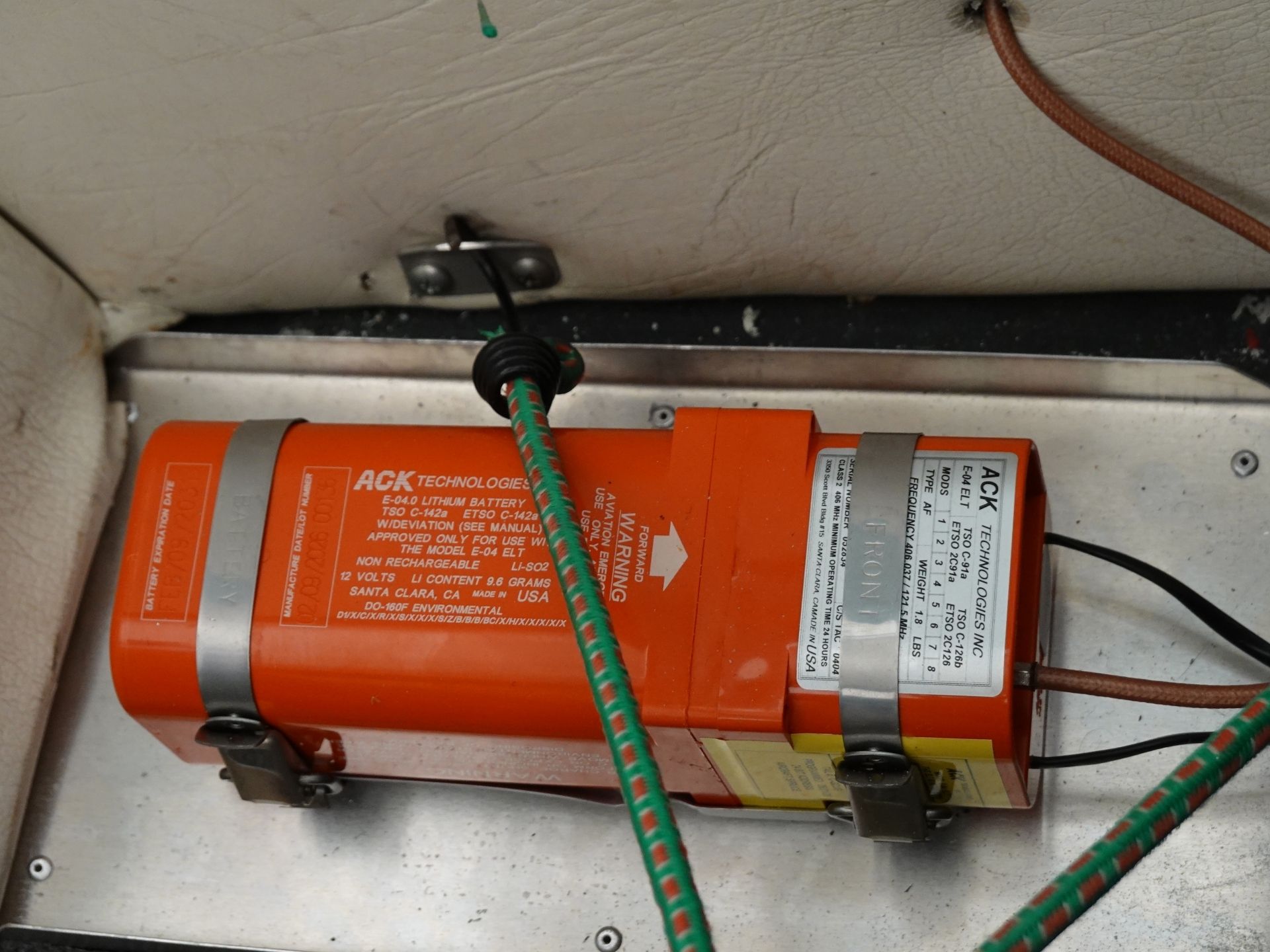 Orange lithium battery module mounted to a metal panel with green and orange wires connected and secured by clamps, in a mechanical compartment of a vessel or cabinet.