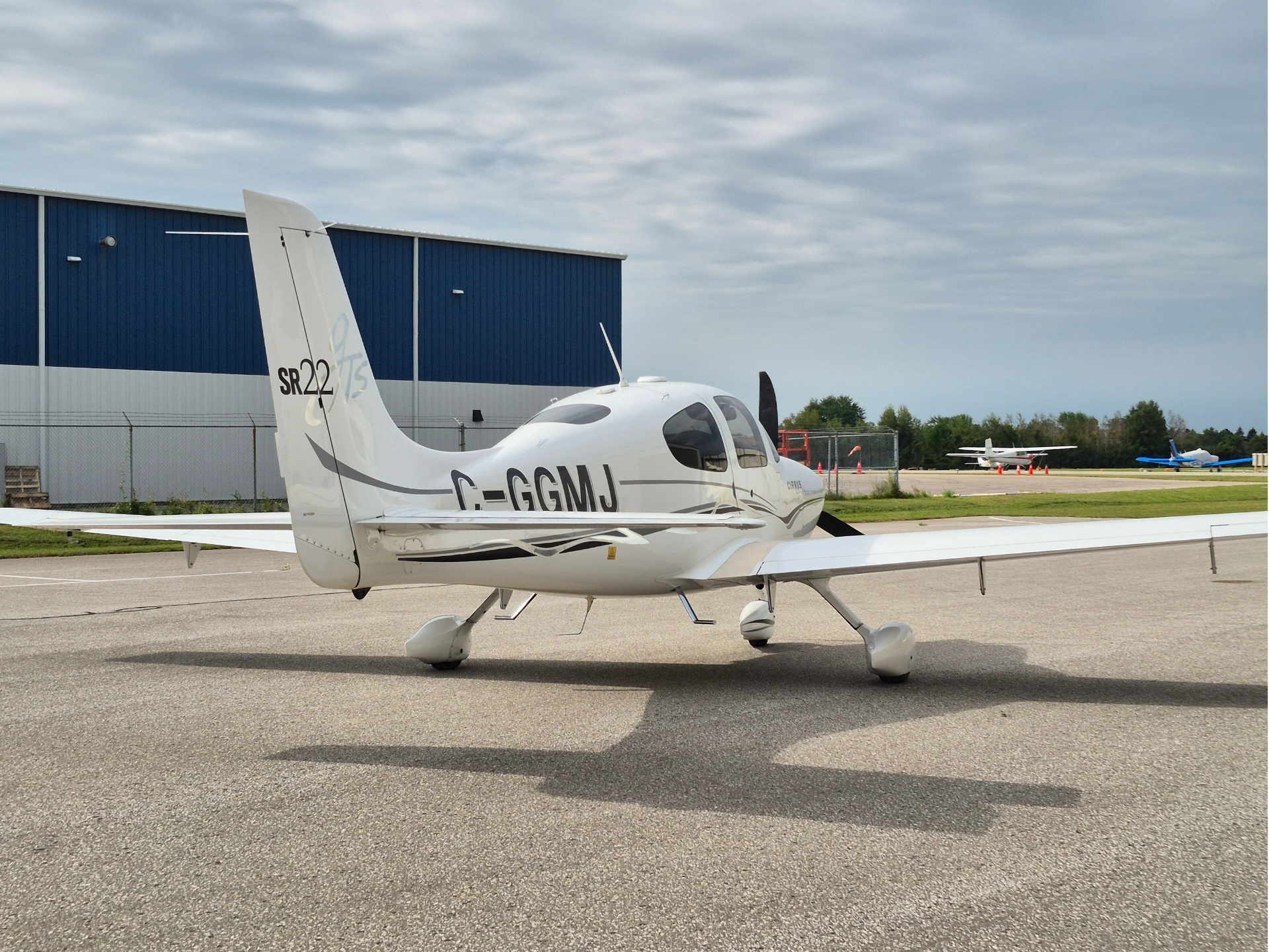 Small white single engine airplane parked on a tarmac with a blue hangar in the background