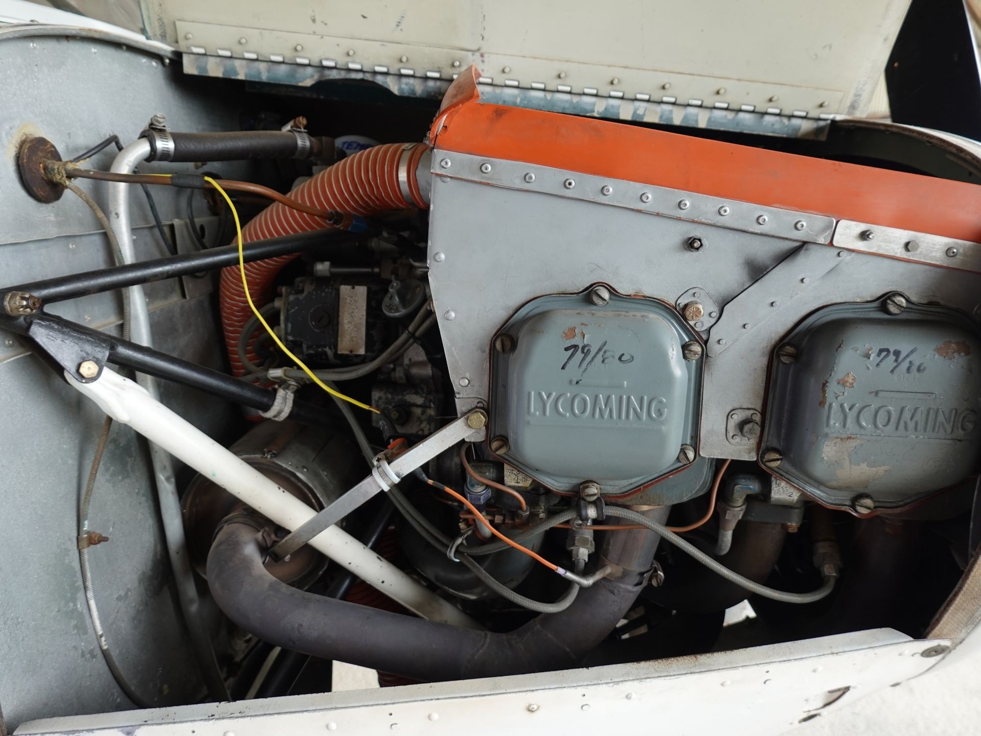 Close-up of a Lycoming aircraft engine inside its metal cowling, with orange intake duct, hoses, and wiring visible