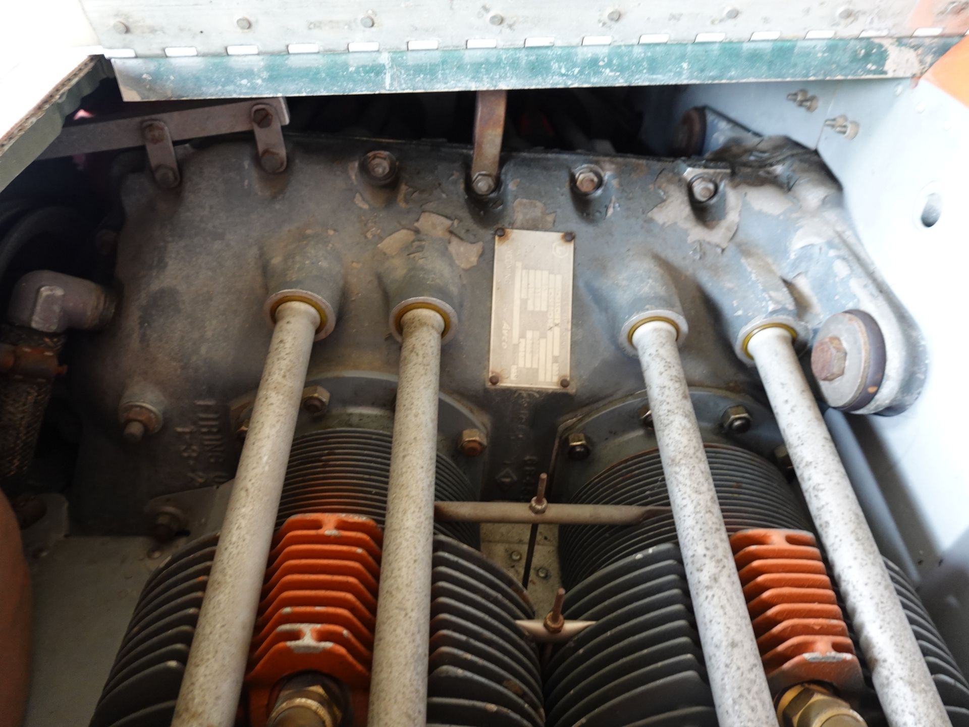 Close-up of an old industrial engine showing vertical exhaust/valve components, rusted bolts, and dusty metal surfaces with a small identification plate in the center digital imageplate area to the right of the rods.
