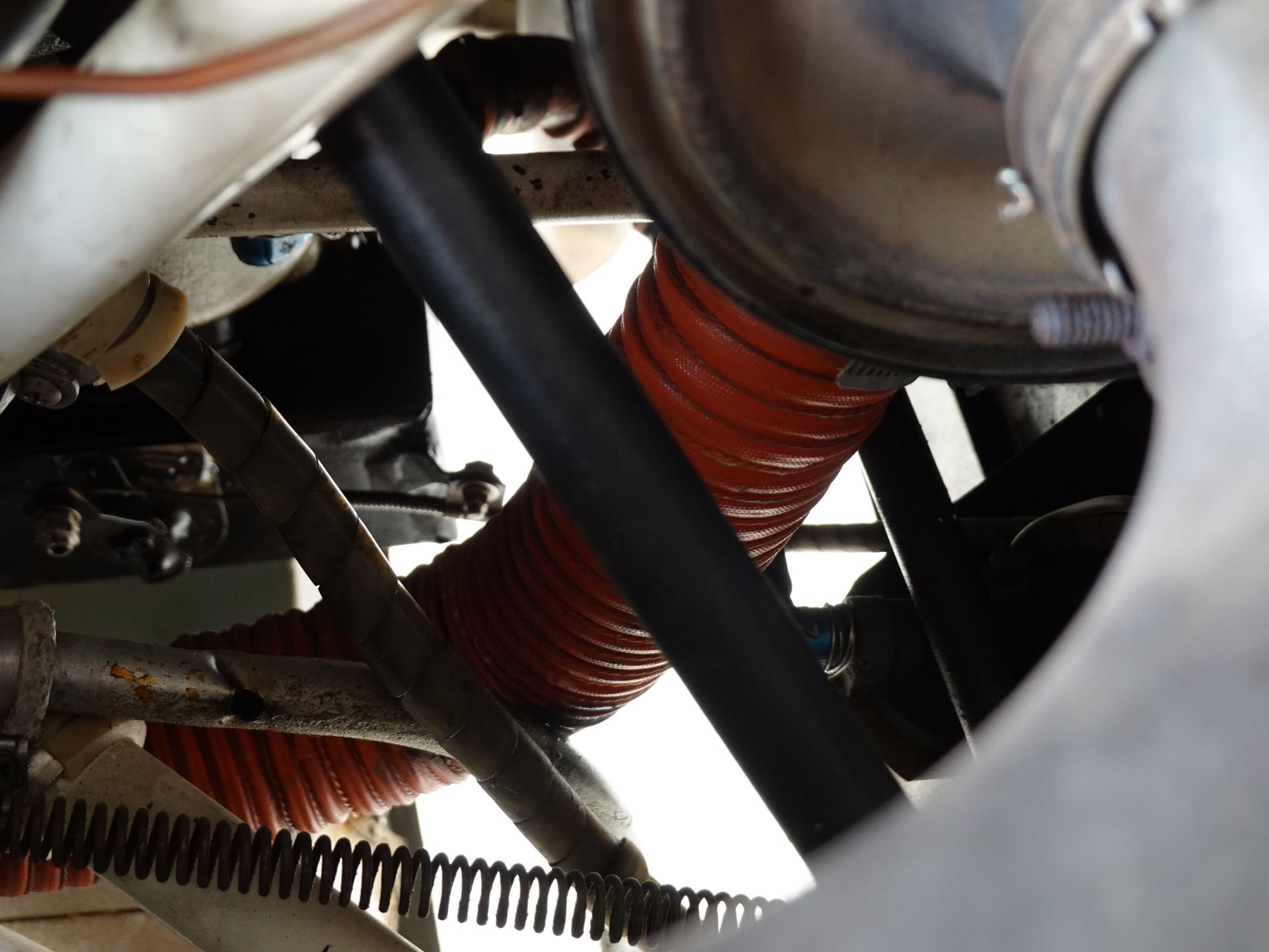 Close-up of a red corrugated hose and black cables inside a dusty industrial machine, viewed from below.