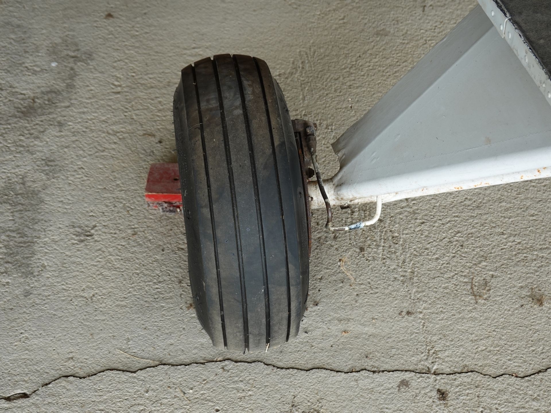 A single black tire with four deep grooves attached to a metal landing gear leg on a rough concrete surface.