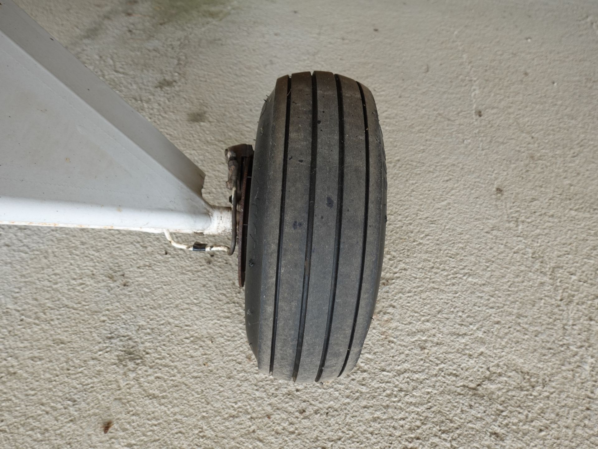 Close-up of a worn black airplane landing gear tire with four grooves, mounted on a metal strut over a textured concrete surface.