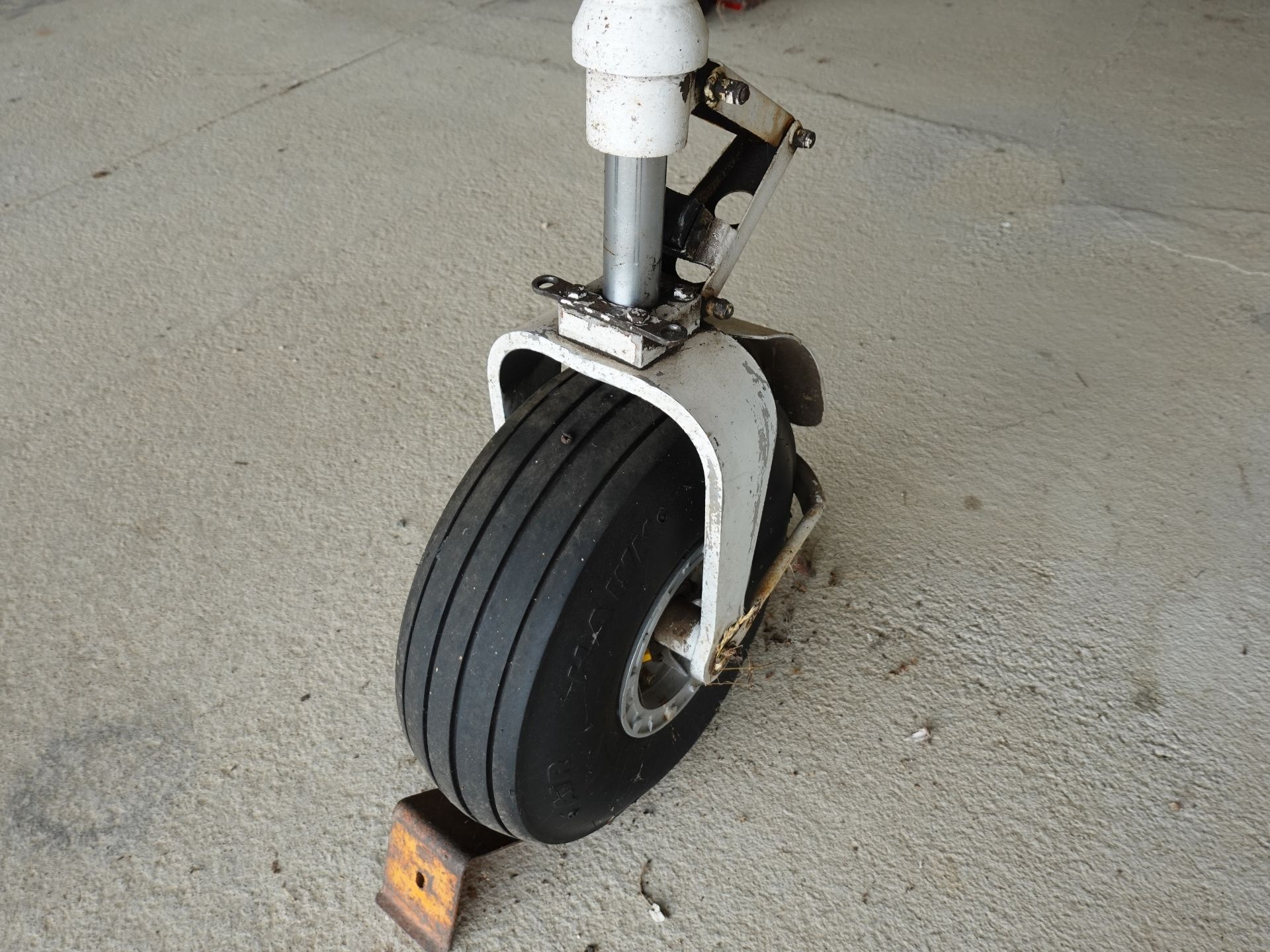 Front wheel and fork of a vintage scooter with a white fender, resting on a rough concrete floor.