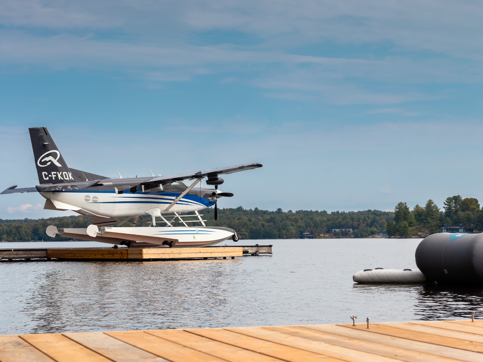 Seaplane on a wooden dock at a lake tail number C FKQK with blue sky and tree lined shore in the background