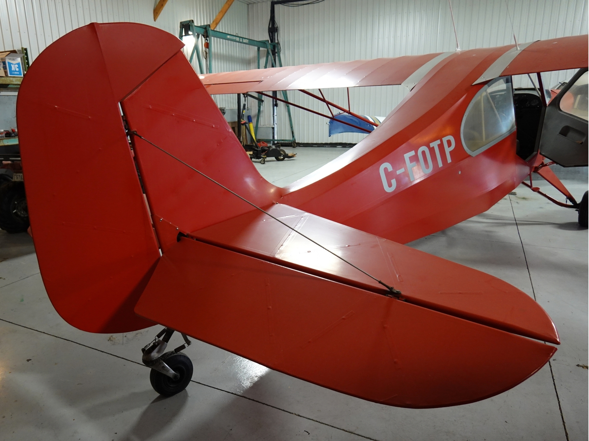Red vintage biplane inside a hangar fuselage marked C FOTP with open cockpit window visible