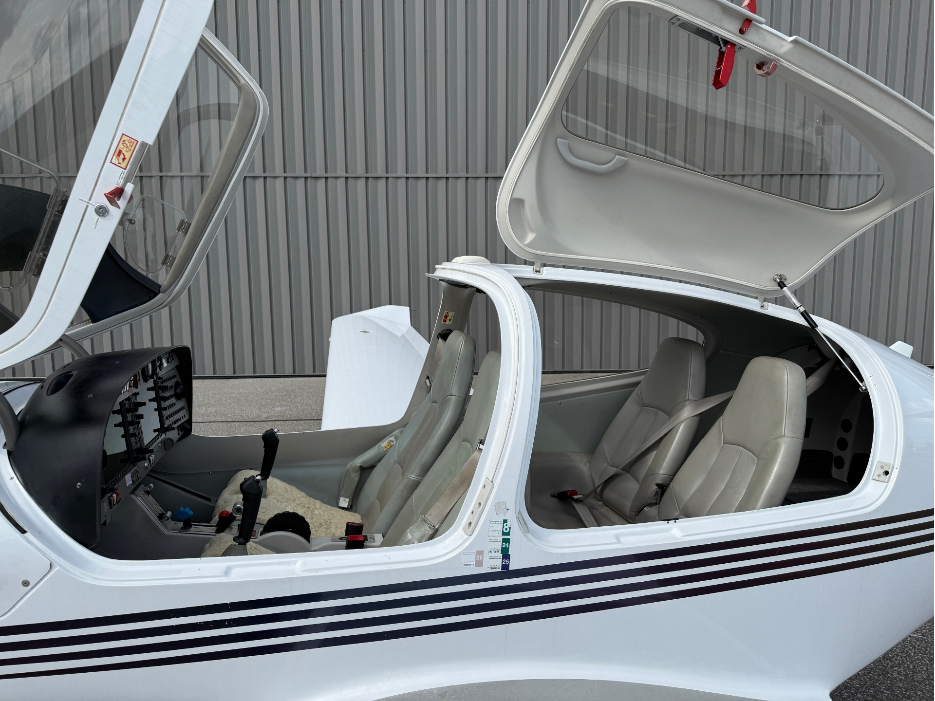 Open cockpit of a small white airplane with gray seats and visible instrument panel, hangar wall in the background.