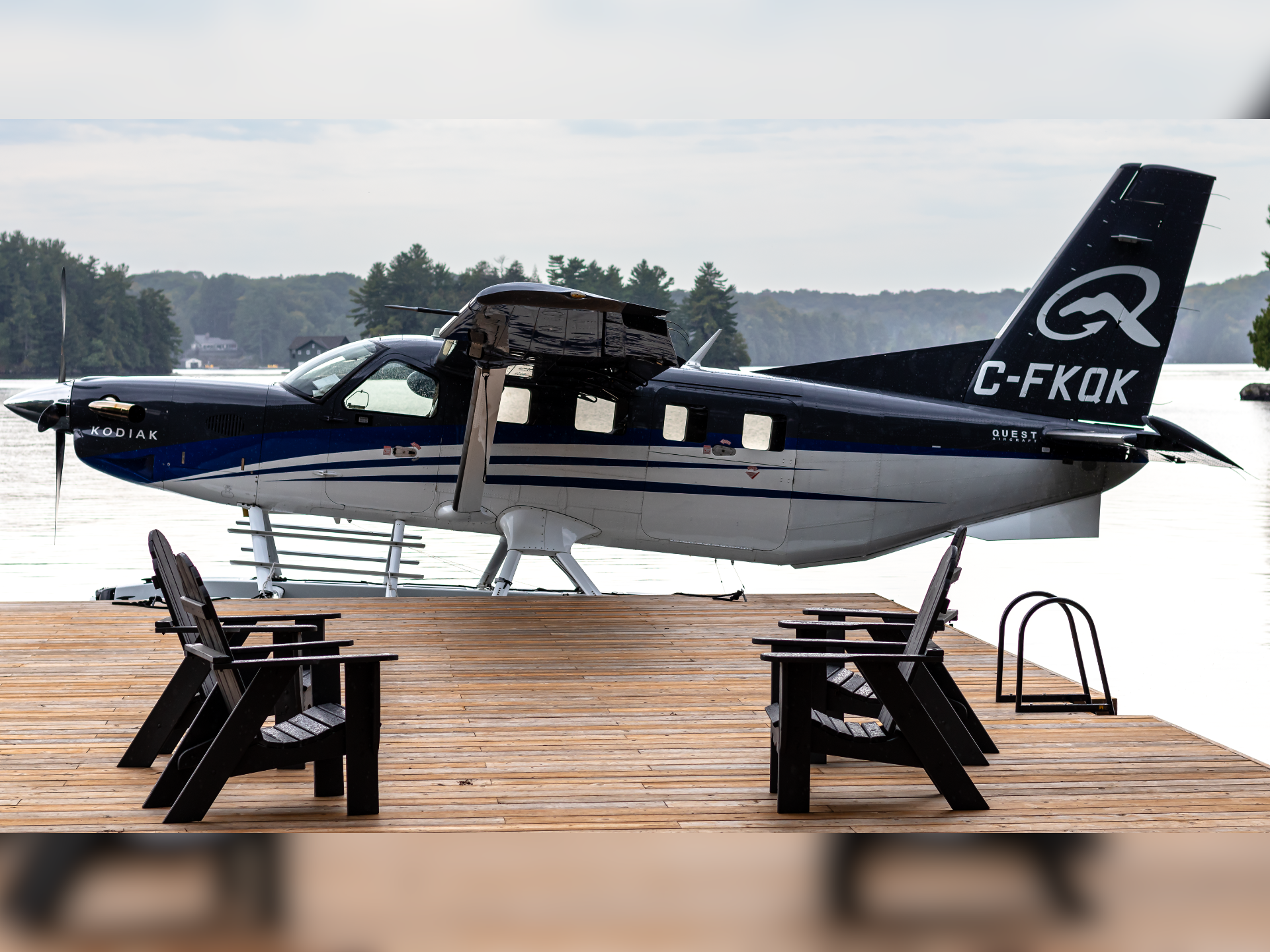 Blue and black Kodiak seaplane on a wooden dock by a lake outdoor tables and chairs nearby