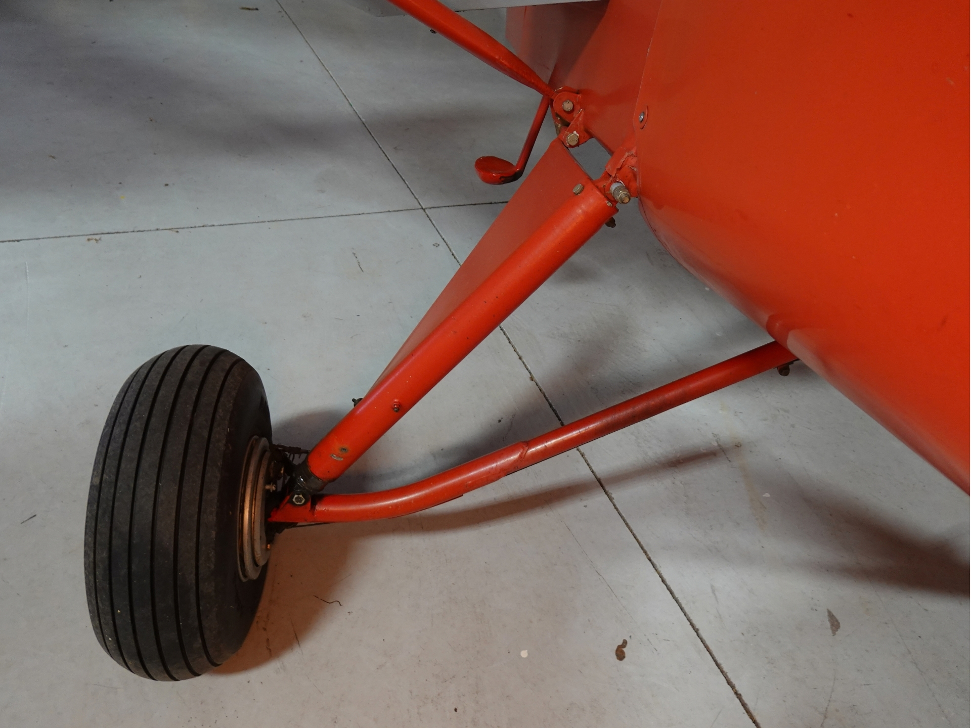 Red aircraft landing gear with a black tire on a gray concrete floor close up view of the wheel and strut