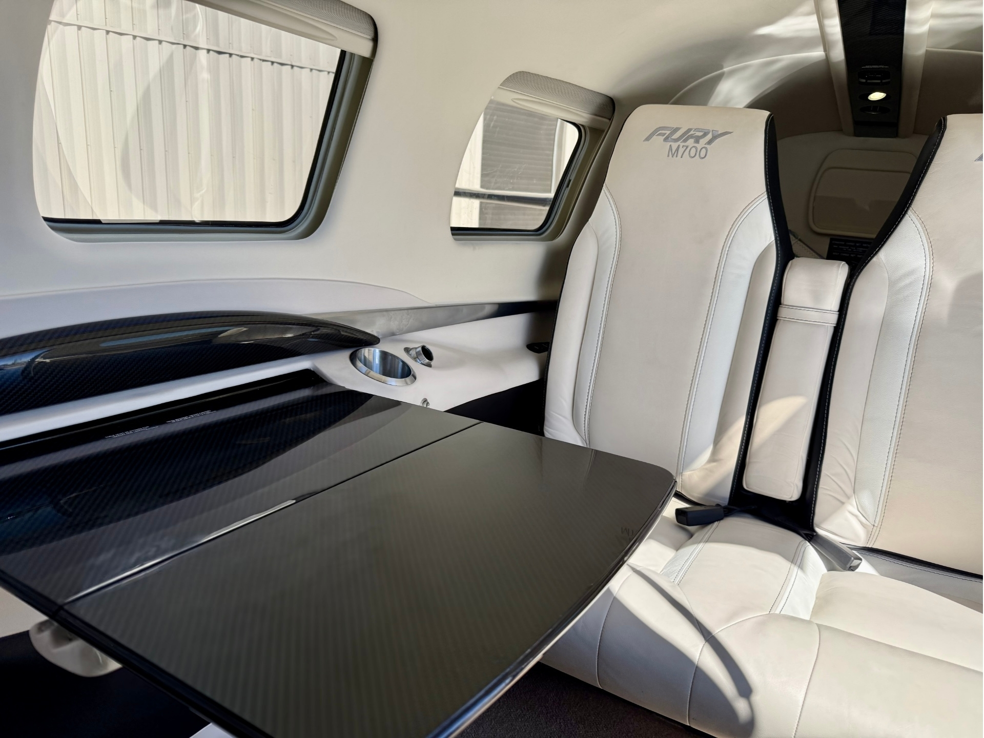 Rear passenger cabin of a Fury M700 white leather captain seats with black piping and a carbon fiber table nearby