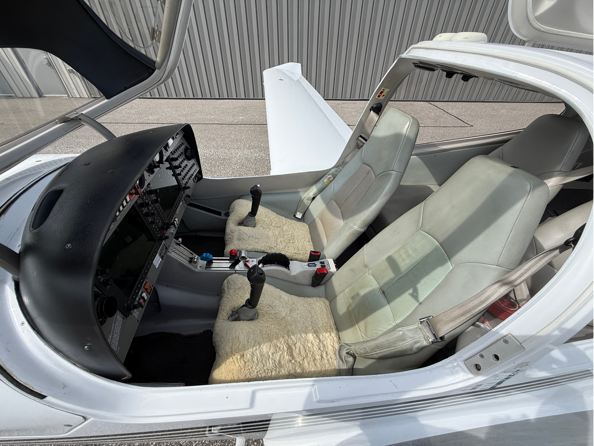 Open-cockpit of small airplane showing dual seats, control panel, and beige sheepskin floor mat.
