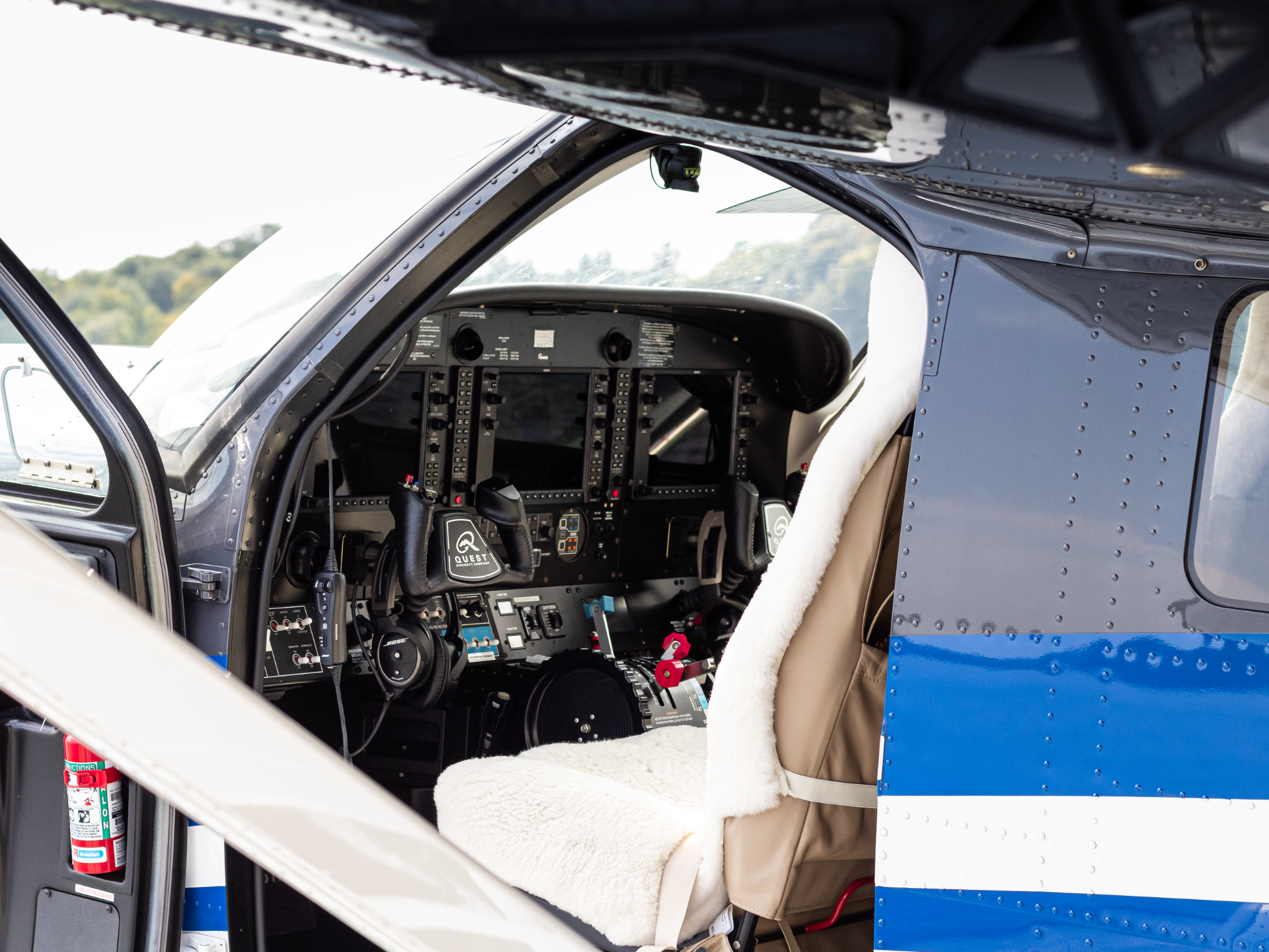 Interior of a small airplane cockpit with control yokes panels and many switches beige seat with a white fluffy cover visible