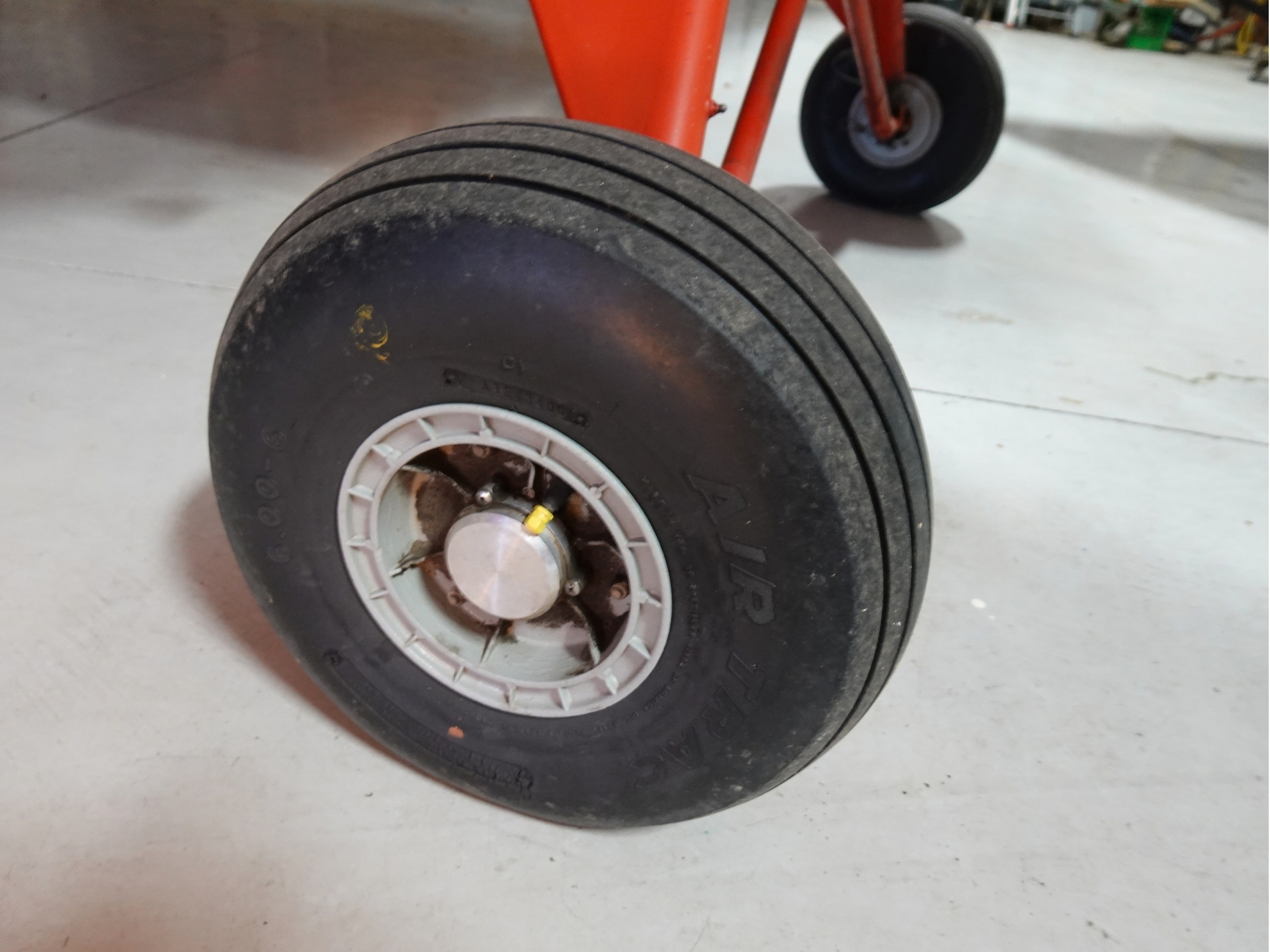 Close up of a large black wheel with a white hub on a red framed cartdolly resting on a concrete floor in a workshop