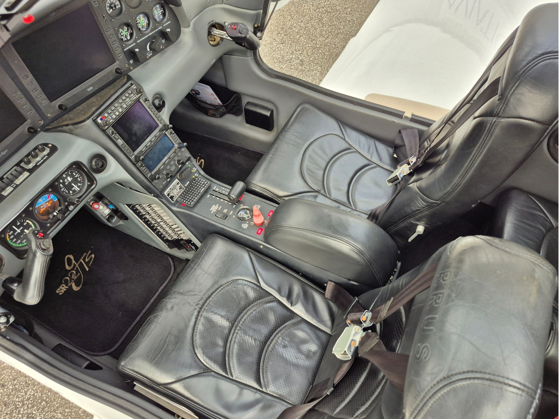 Cockpit interior of a small aircraft with dual seats yoke and instrument panel filled with gauges and screensside view of the controls and throttle