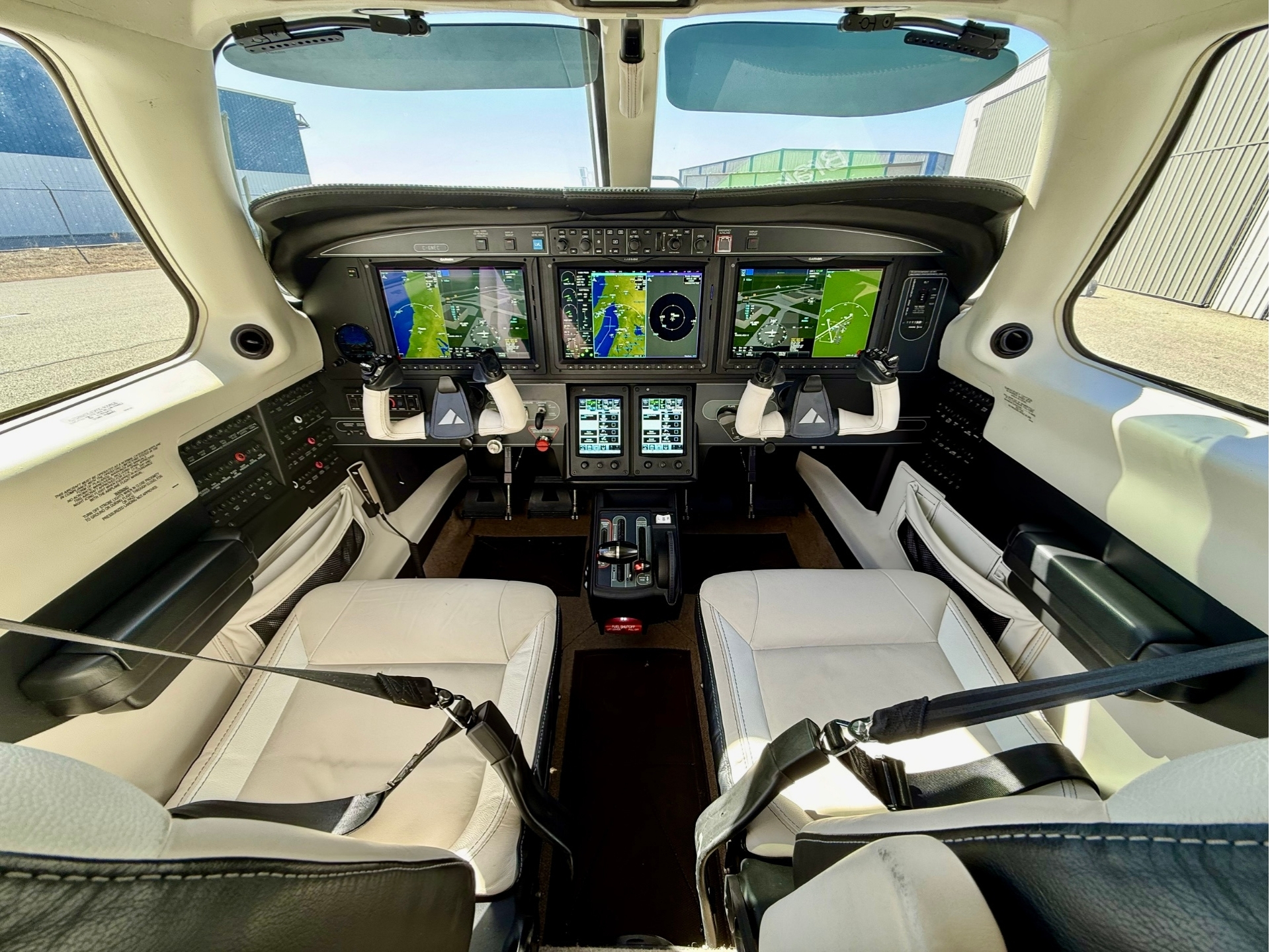 Modern aircraft cockpit with four large touchscreen flight displays dual yokes and white leather seats