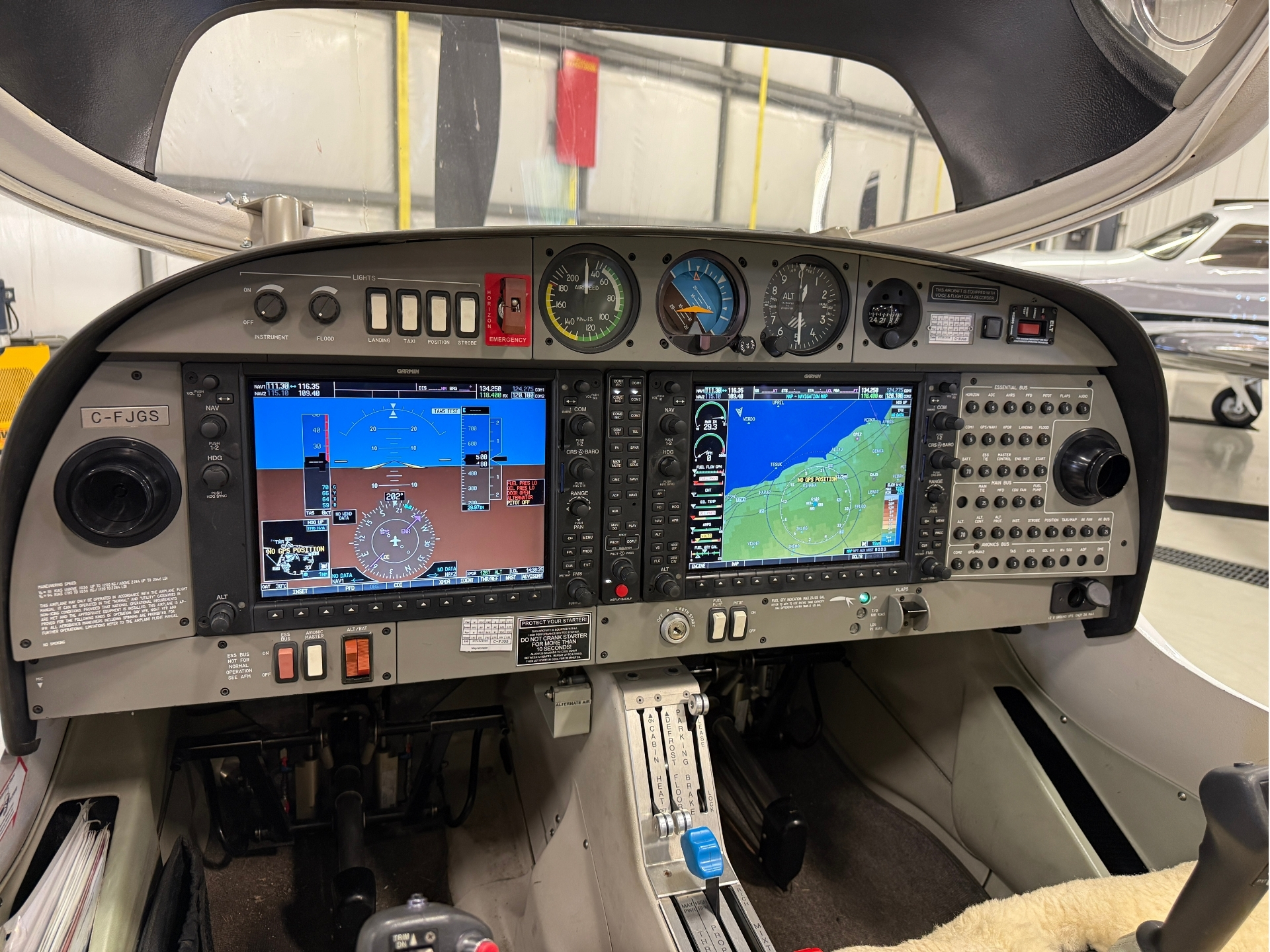 Cockpit view of a small aircraft with dual large navigation screens and assorted gauges on the instrument panel next to the flight controls.