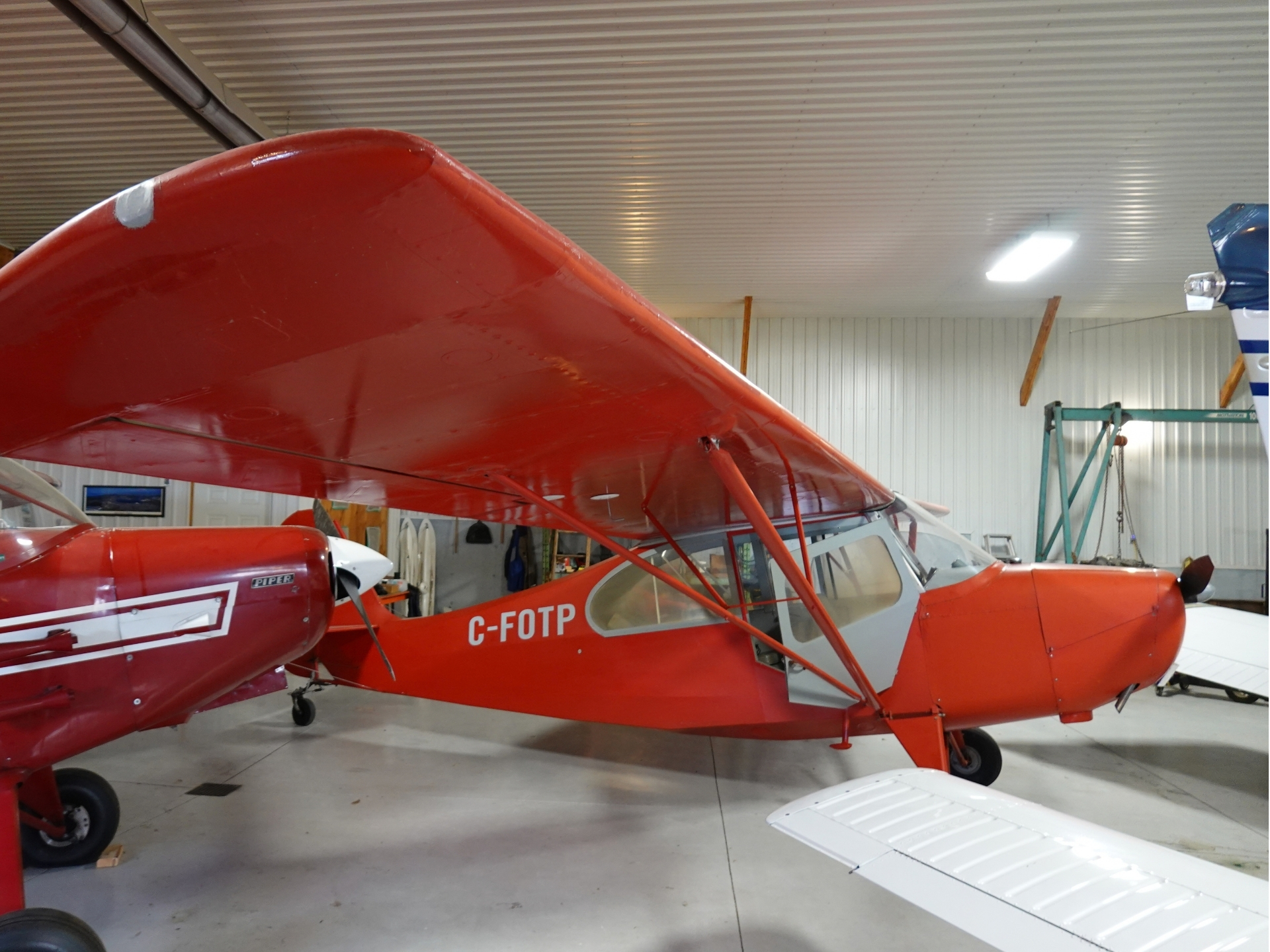 Red light aircraft inside a hangar large red wing overhead with C FOTP on the fuselage other planes in the background