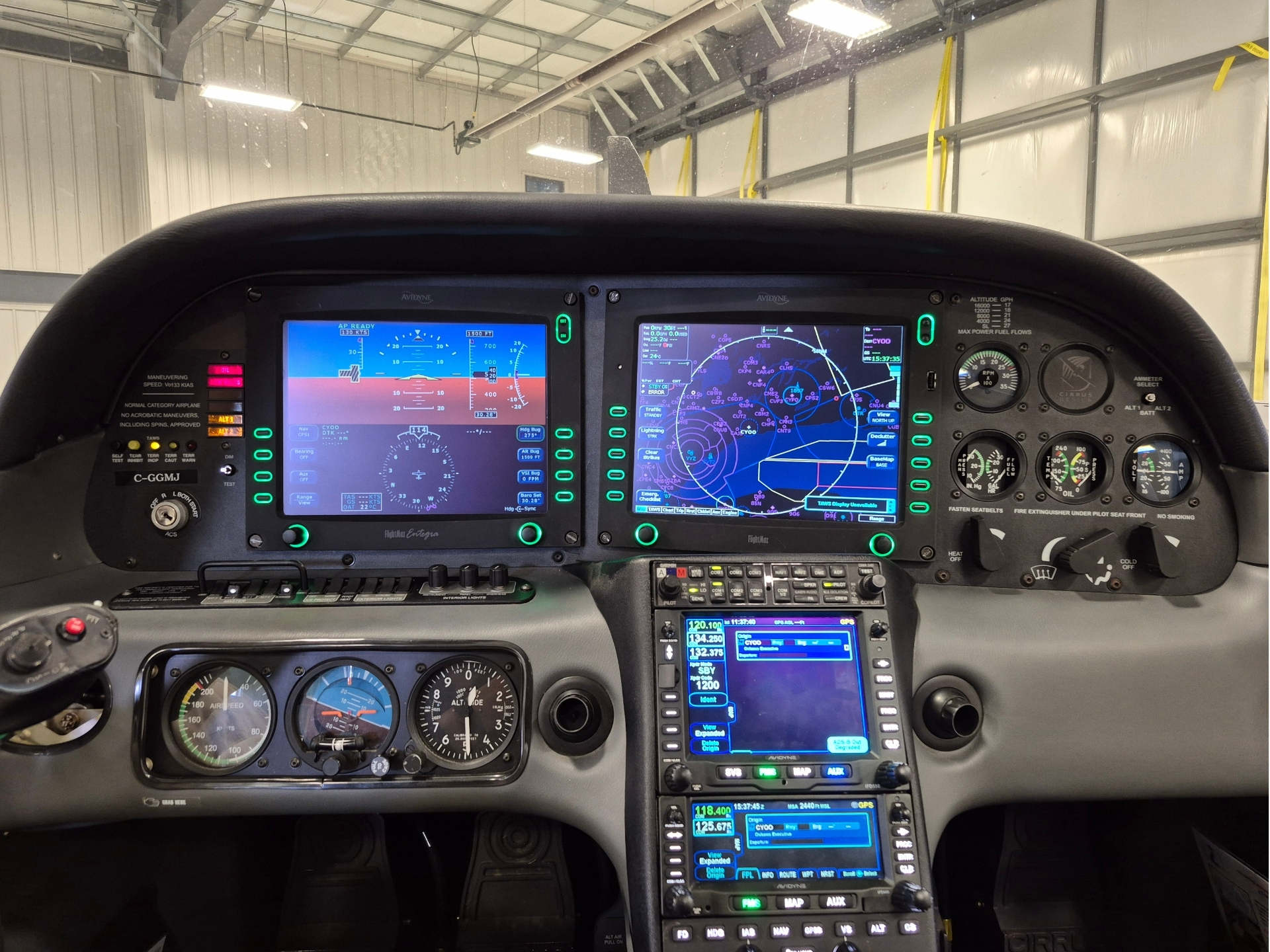 Cockpit dashboard with three large flight display screens and multiple gauges knobs and controls inside a hangar